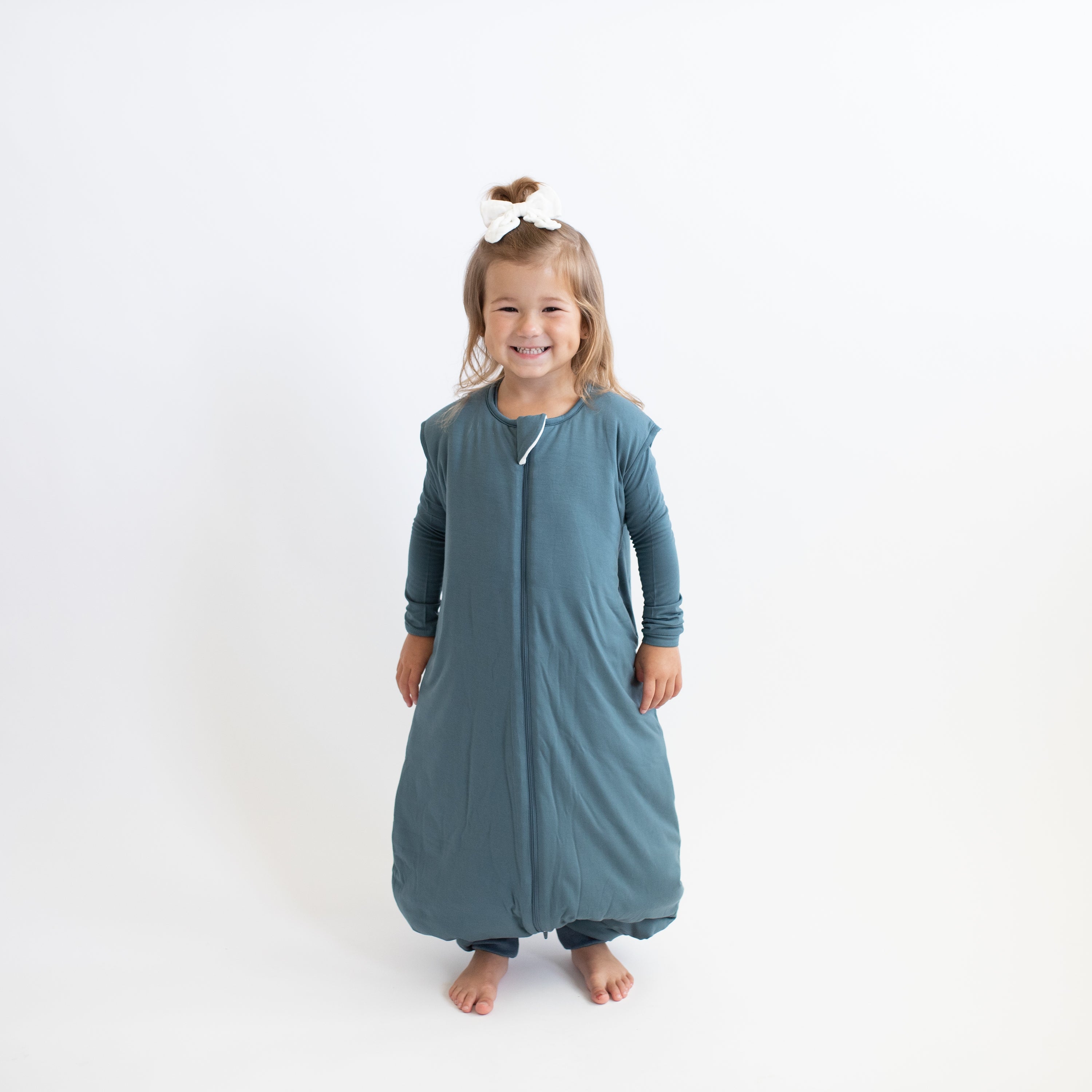 Smiling girl wearing the Sleep Bag Walker in Atlantic 2.5 with matching long sleeve toddler pajamas on underneath