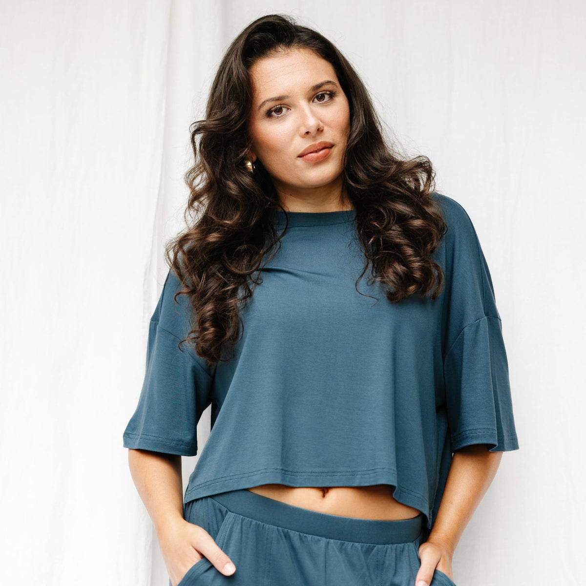 Female model wearing the Women's Short Sleeve Tee in Atlantic standing in front of a white wall