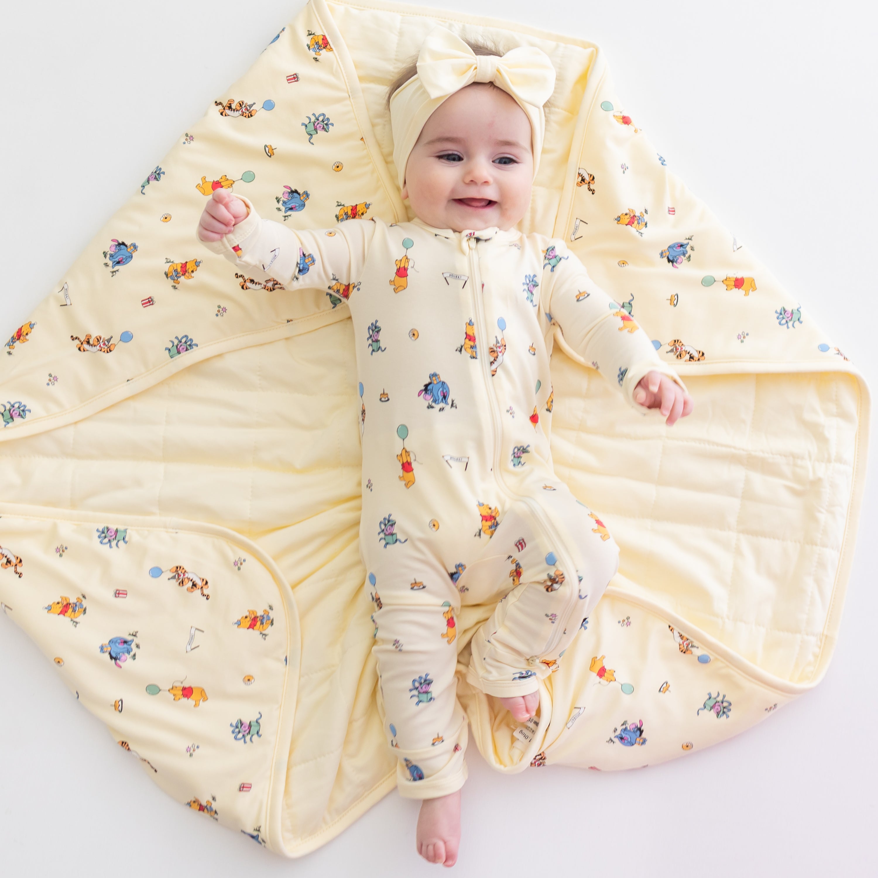 Infant girl laying on a Baby Blanket in Winnie the Pooh Celebration wearing a matching zippered romper