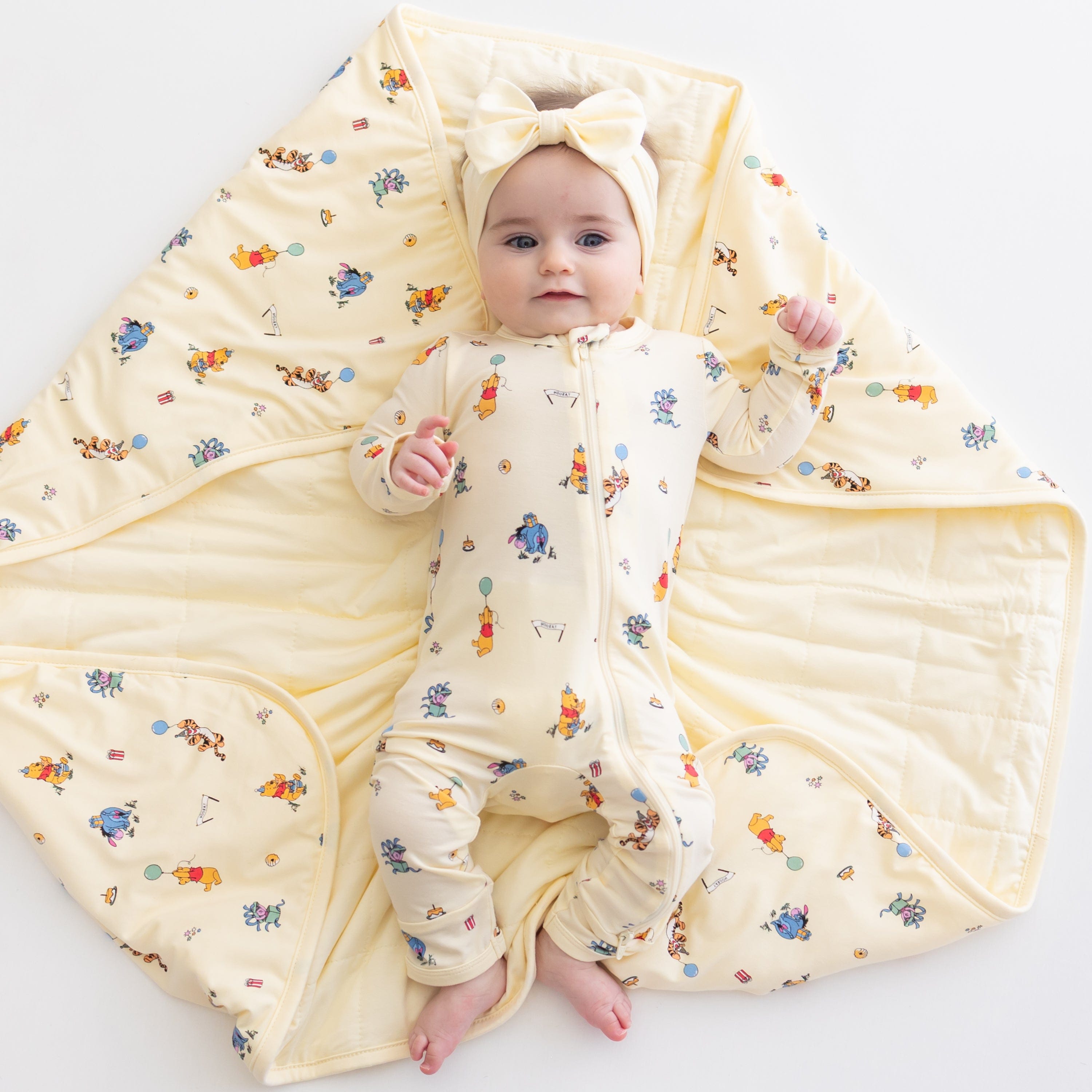 Close up of infant girl laying on a Baby Blanket in Winnie the Pooh Celebration wearing a matching zippered romper