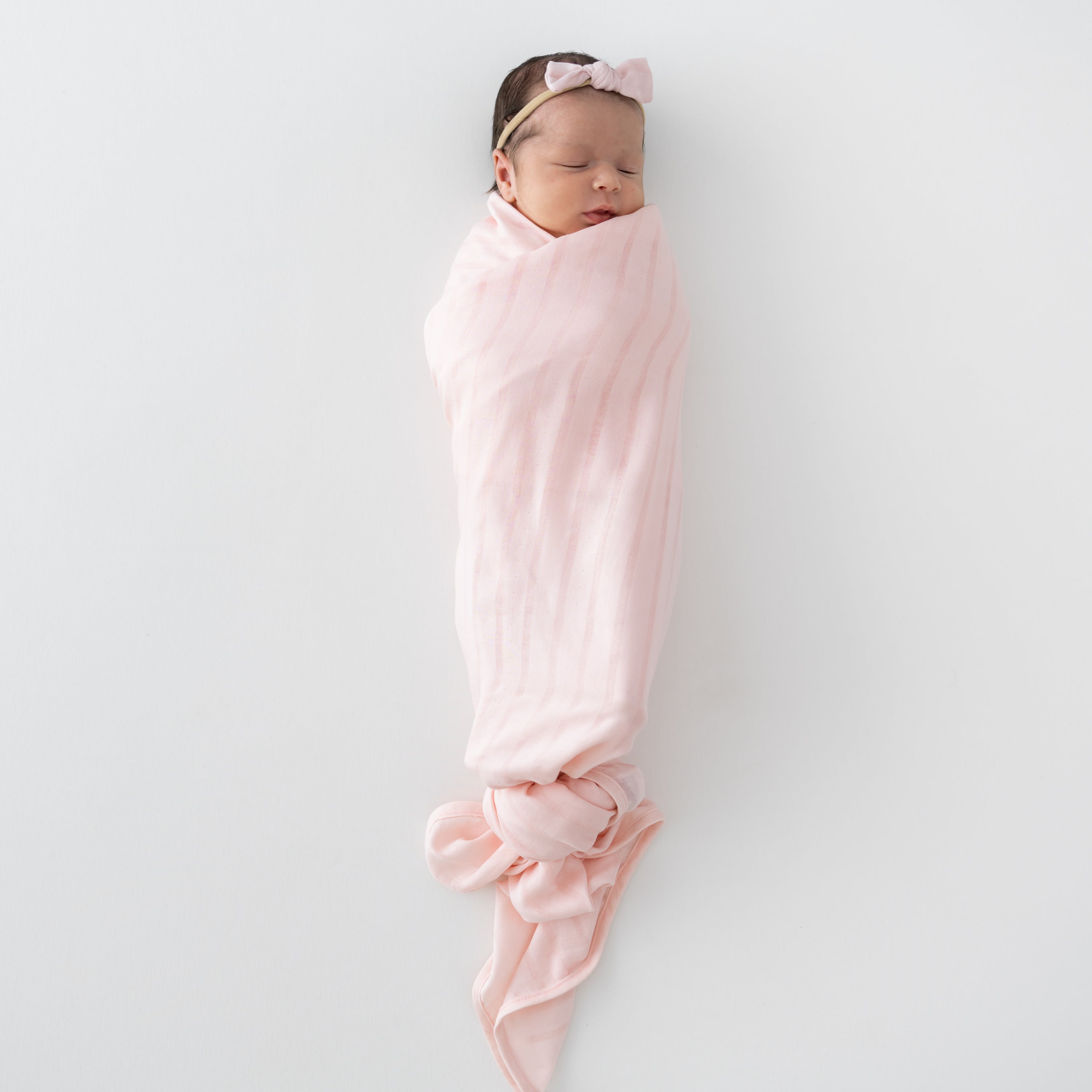 Baby swaddled in Bamboo Muslin Swaddle Blanket in Ballet Pink with Matching Bow