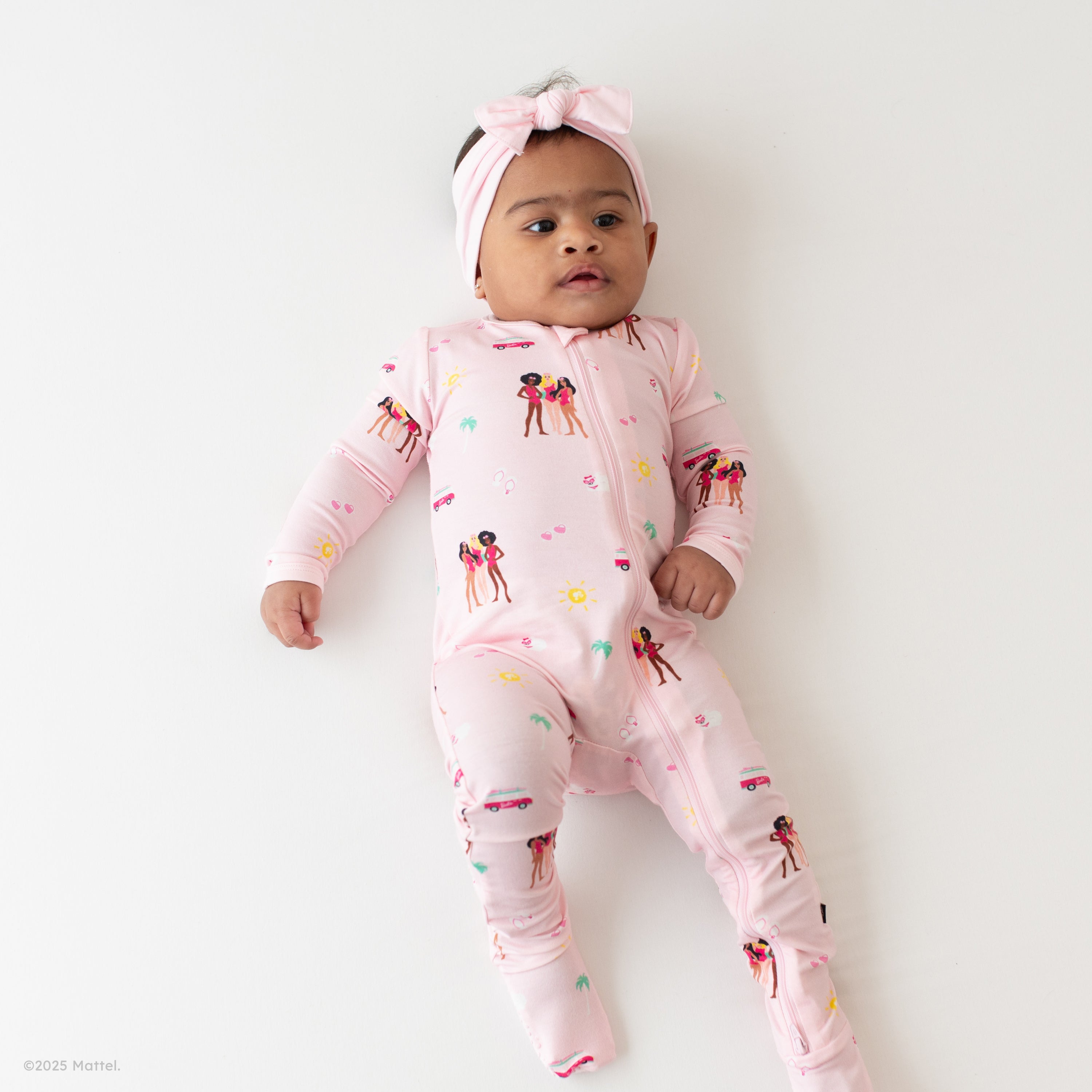 Infant wearing Kyte Baby Zippered Footie in Barbie™ Beach and Sakura bow