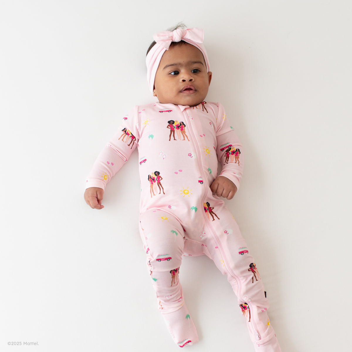 Infant wearing Kyte Baby Zippered Footie in Barbie™ Beach and Sakura bow