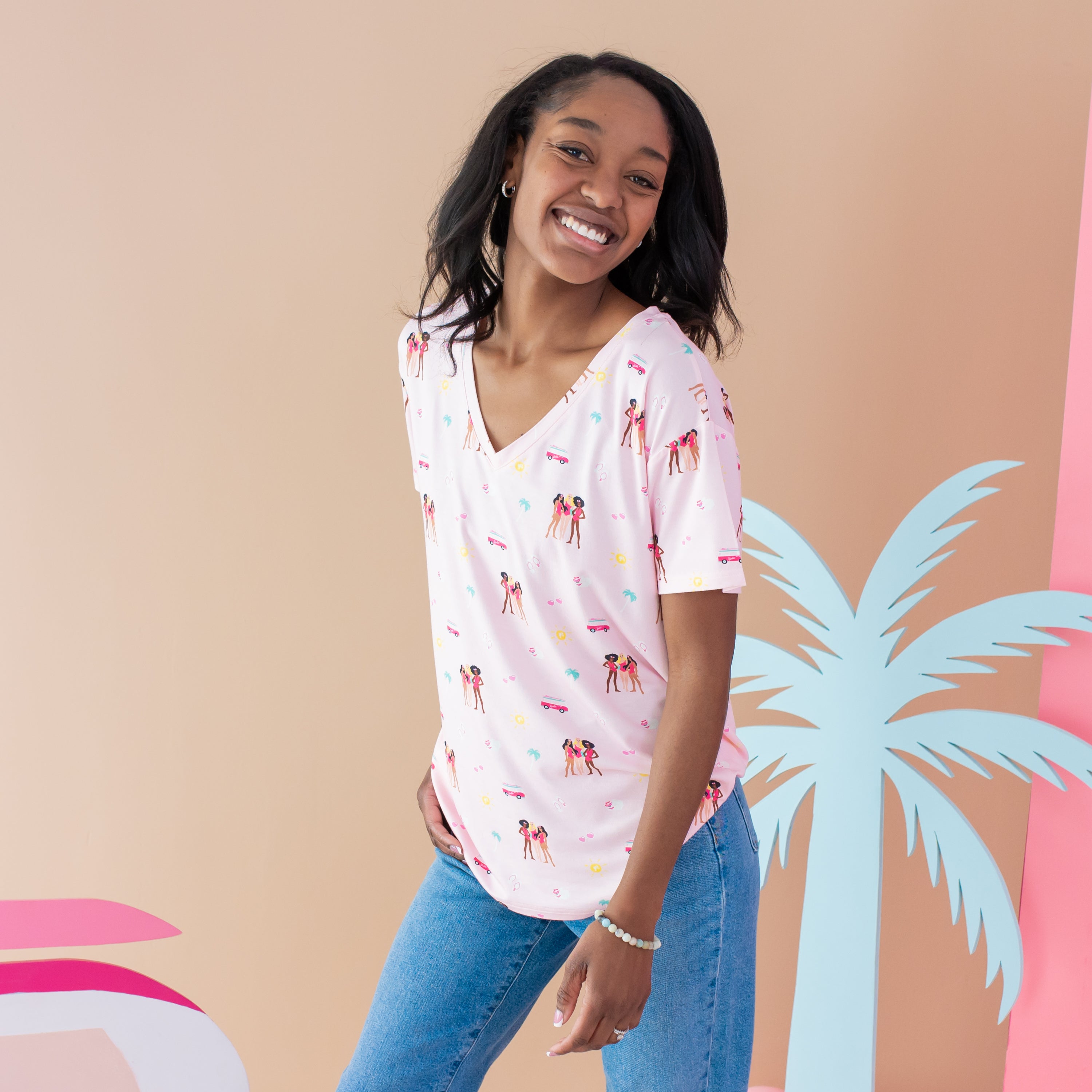 Woman modeling Women's V-Neck Tee in Barbie™ Beach with palm tree backdrop