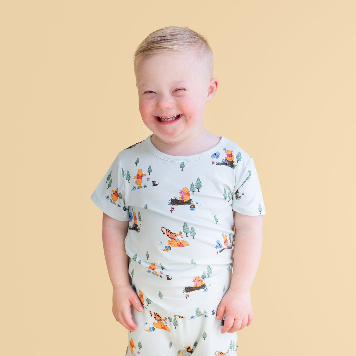 Smiling boy wearing the Toddler Basic Tee in Winnie the Pooh Hundred Acre Wood standing in front of a mustard yellow background