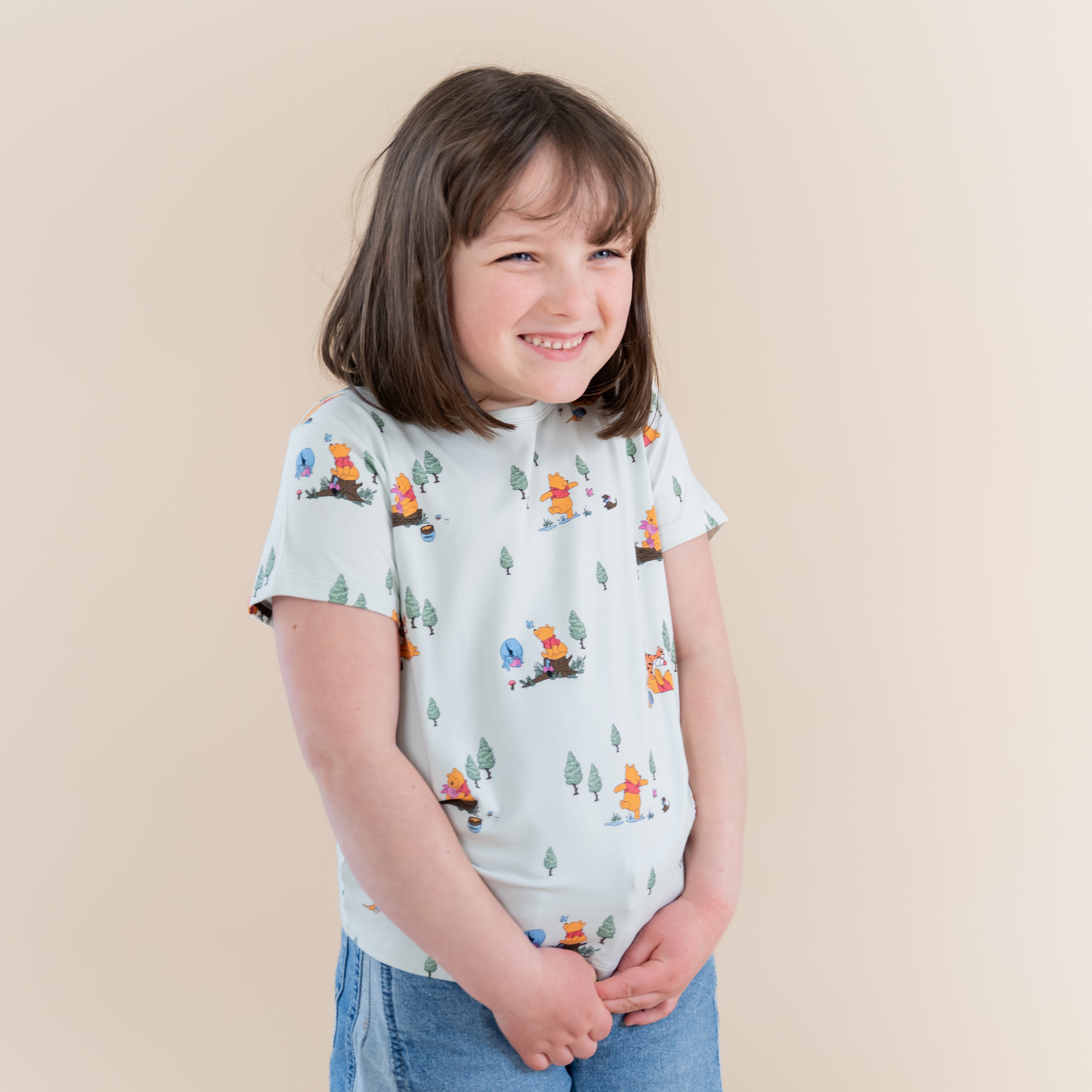 Smiling girl wearing the Toddler Basic Tee in Winnie the Pooh Hundred Acre Wood paired with jean shorts