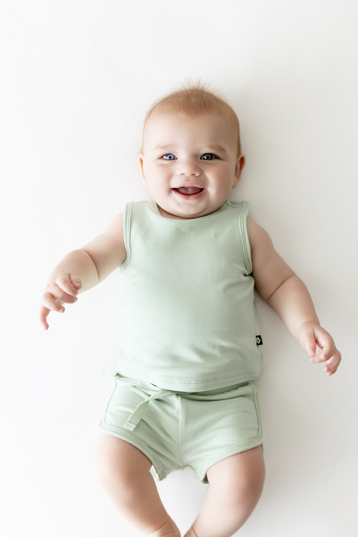 Infant laying on a light surface wearing the Tank Jogger Set in Basil