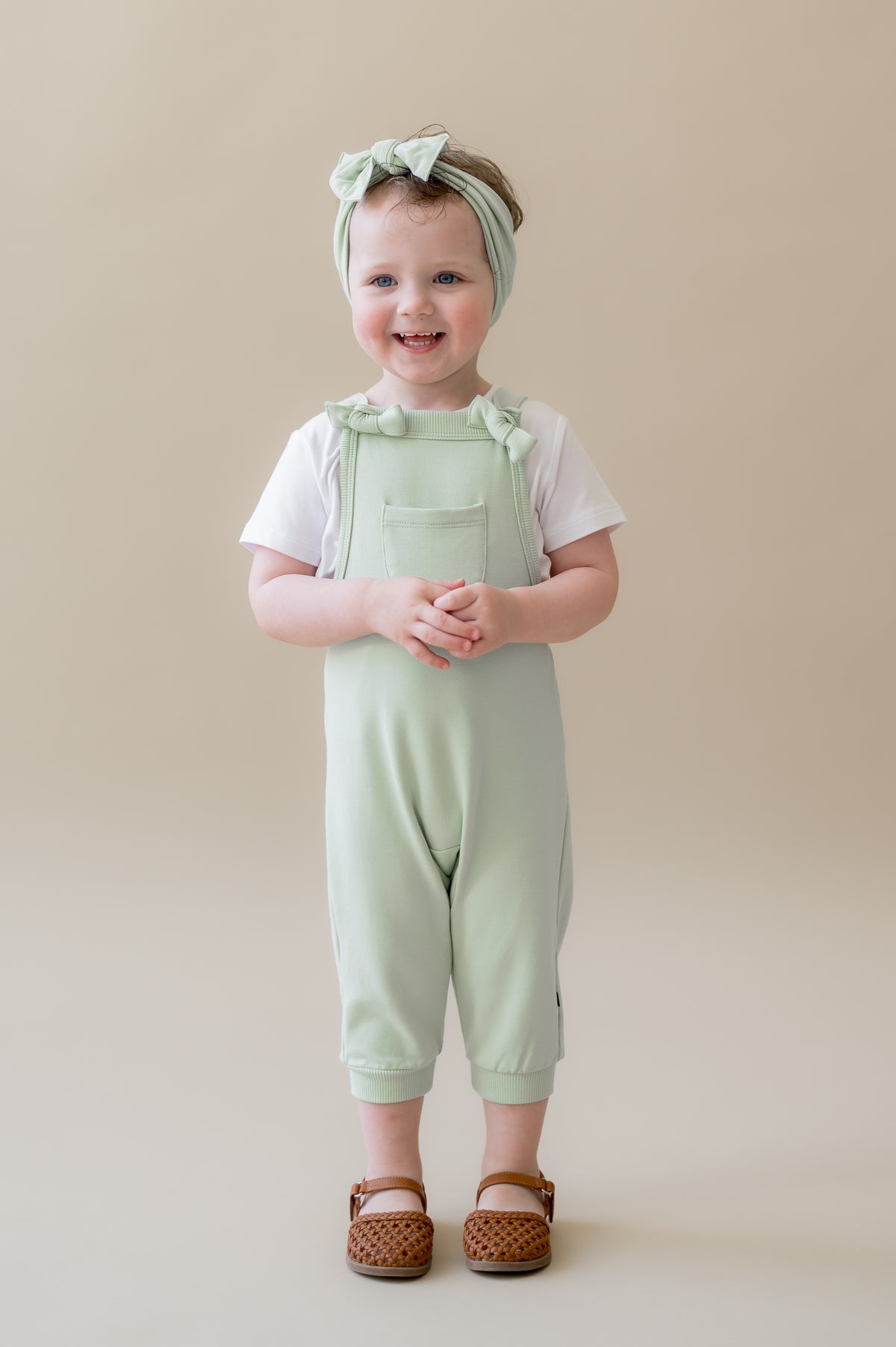 Young girl wearing the Overall in Basil with a white shirt on underneath