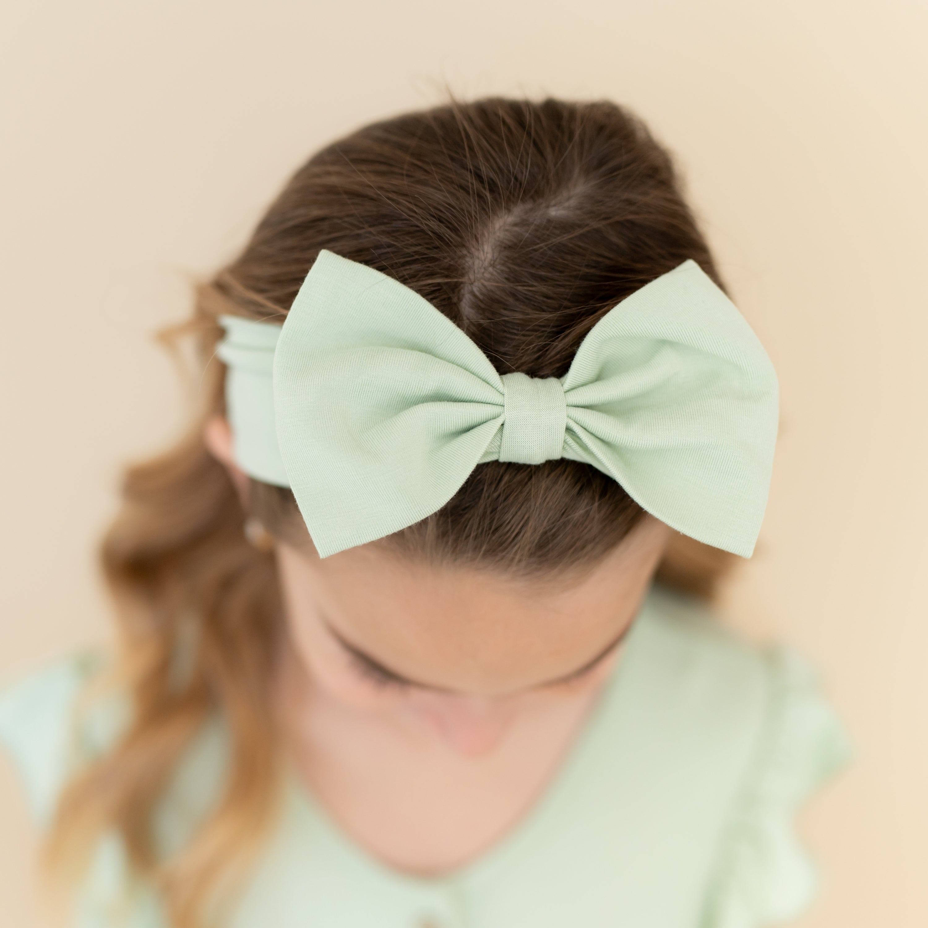 Close up of the Bow Headband in Basil shown on a young girl