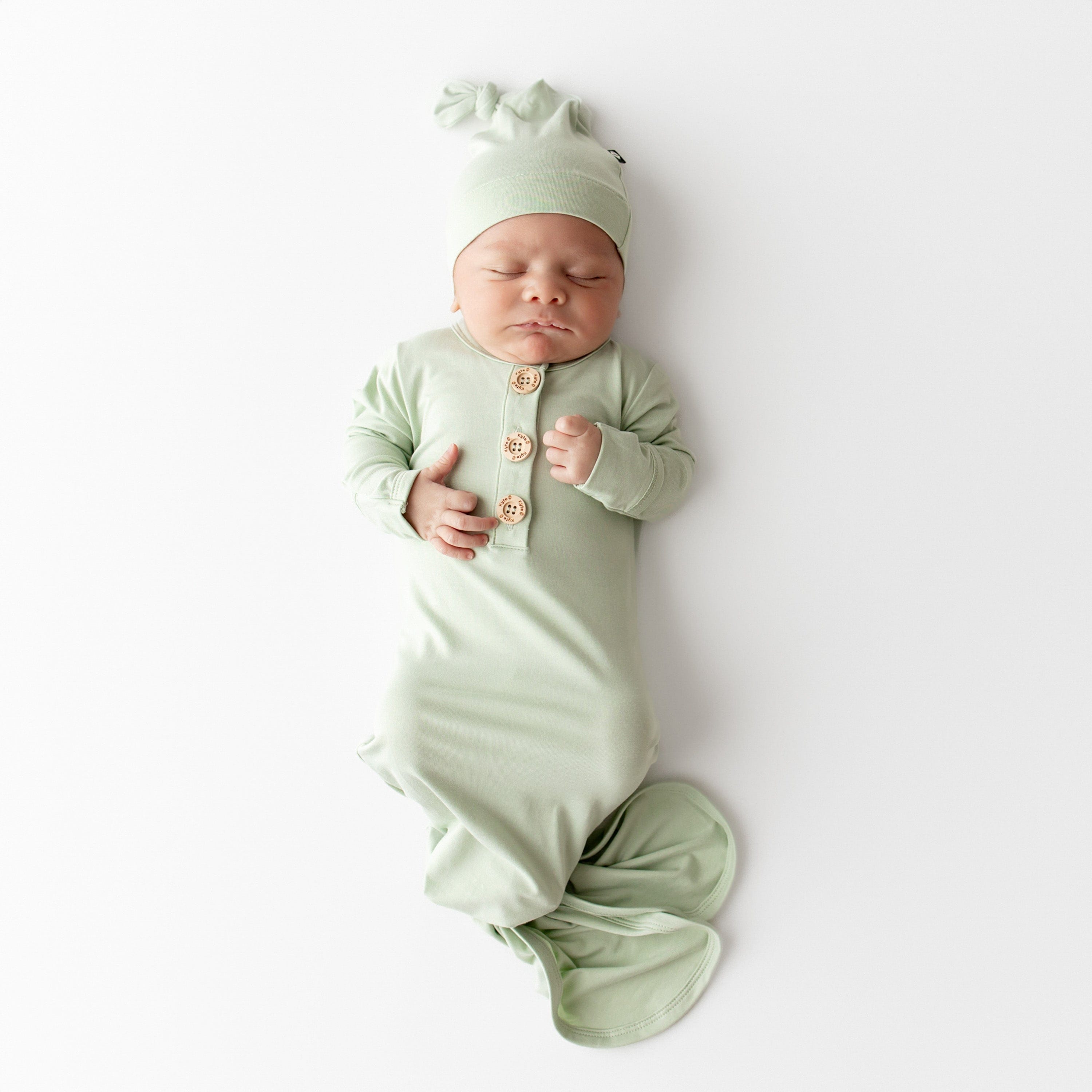 Baby wearing a light green knotted gown and cap set