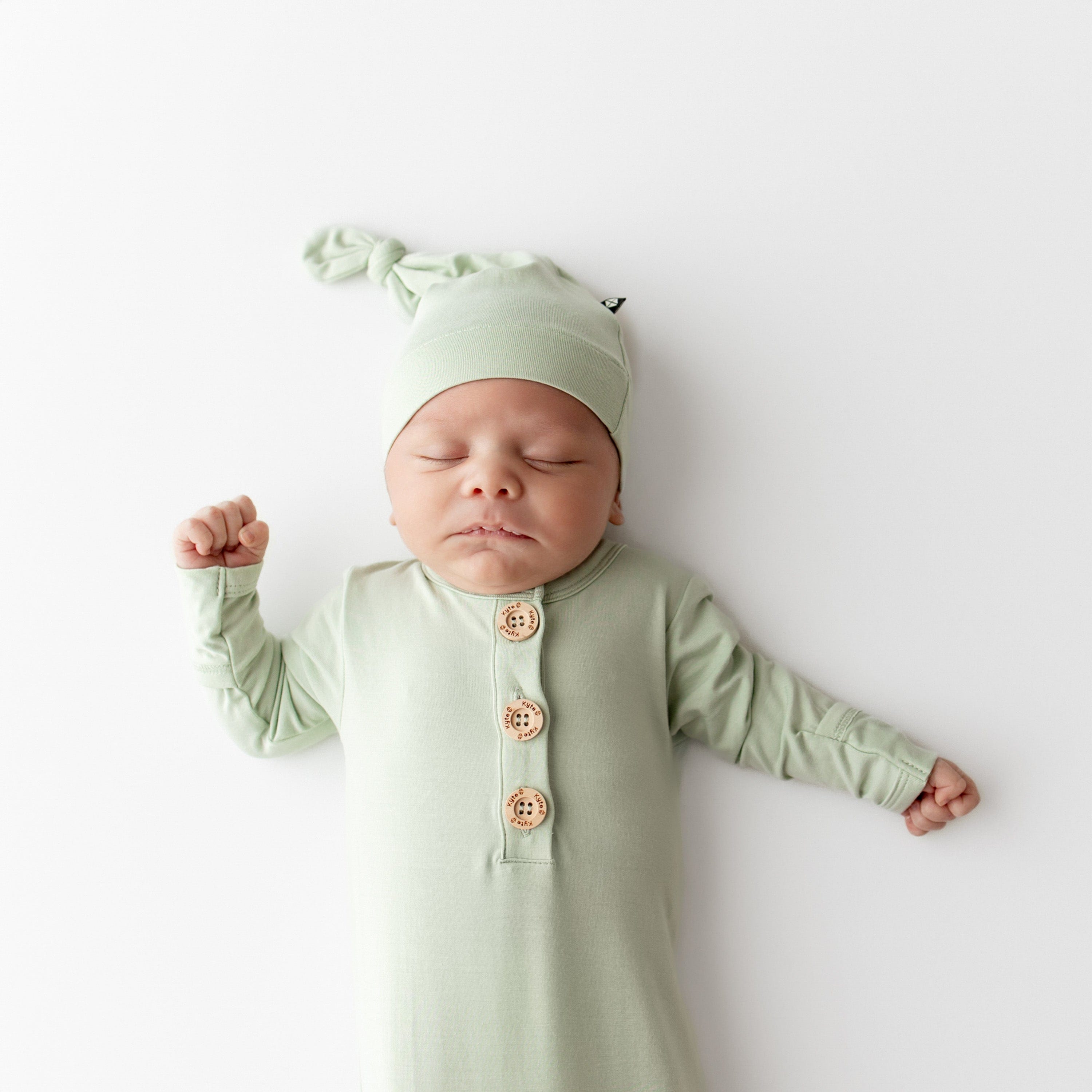 Newborn baby in a green outfit with buttons and matching hat on a white background
