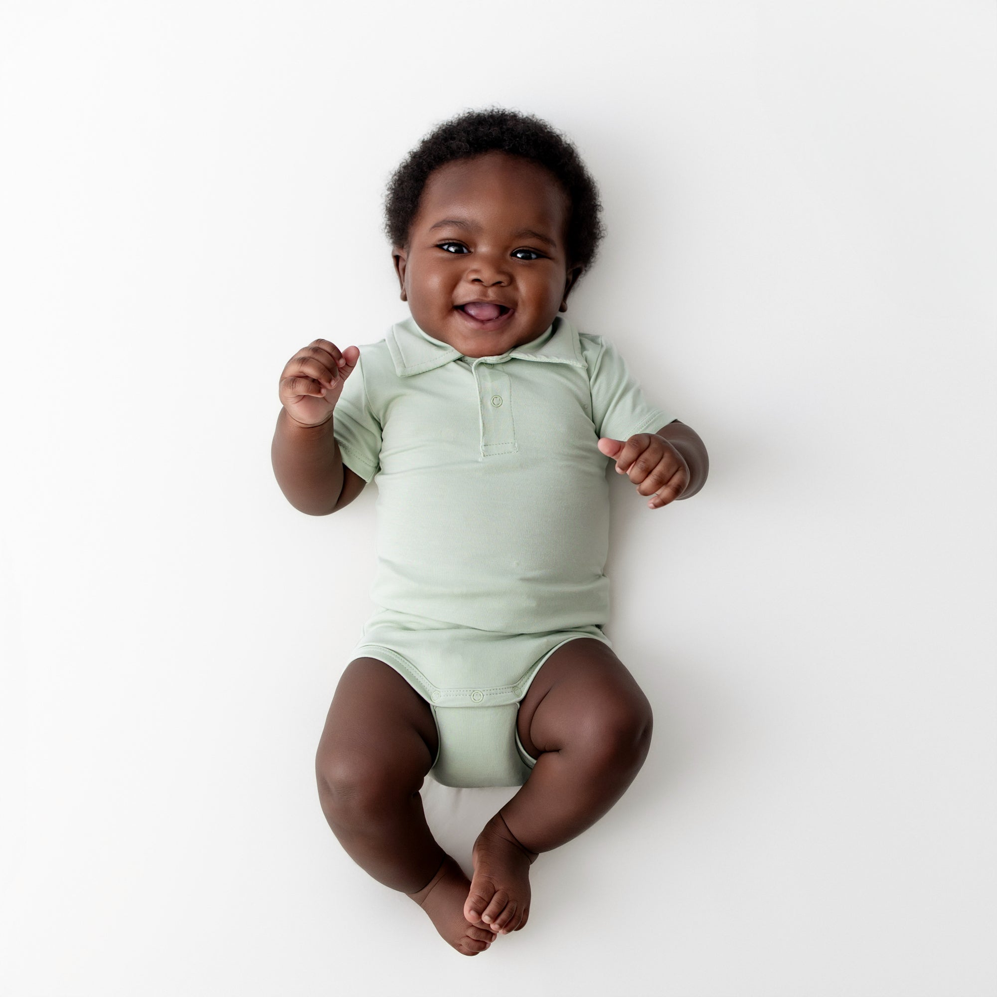 Infant wearing the Polo Bodysuit in Basil laying on a light neutral surface