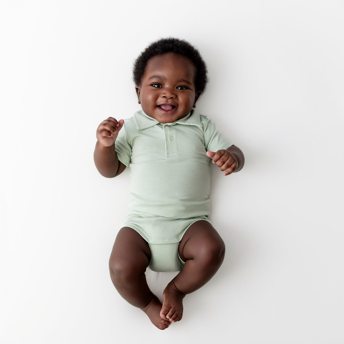 Infant wearing the Polo Bodysuit in Basil laying on a light neutral surface