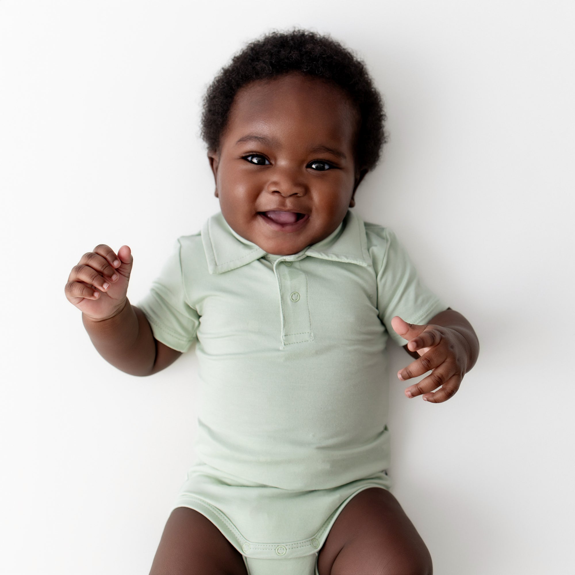 Close up of infant wearing the Polo Bodysuit in Basil on a light neutral surface