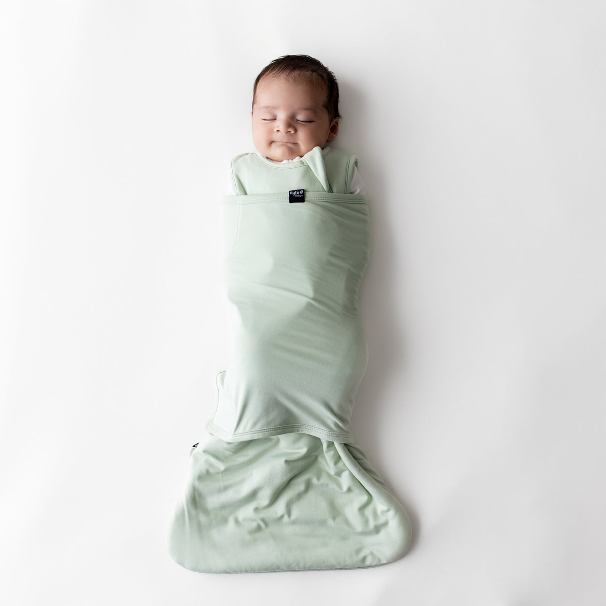Sleeping newborn swaddled in the Sleep Bag Swaddler in Basil 1.0