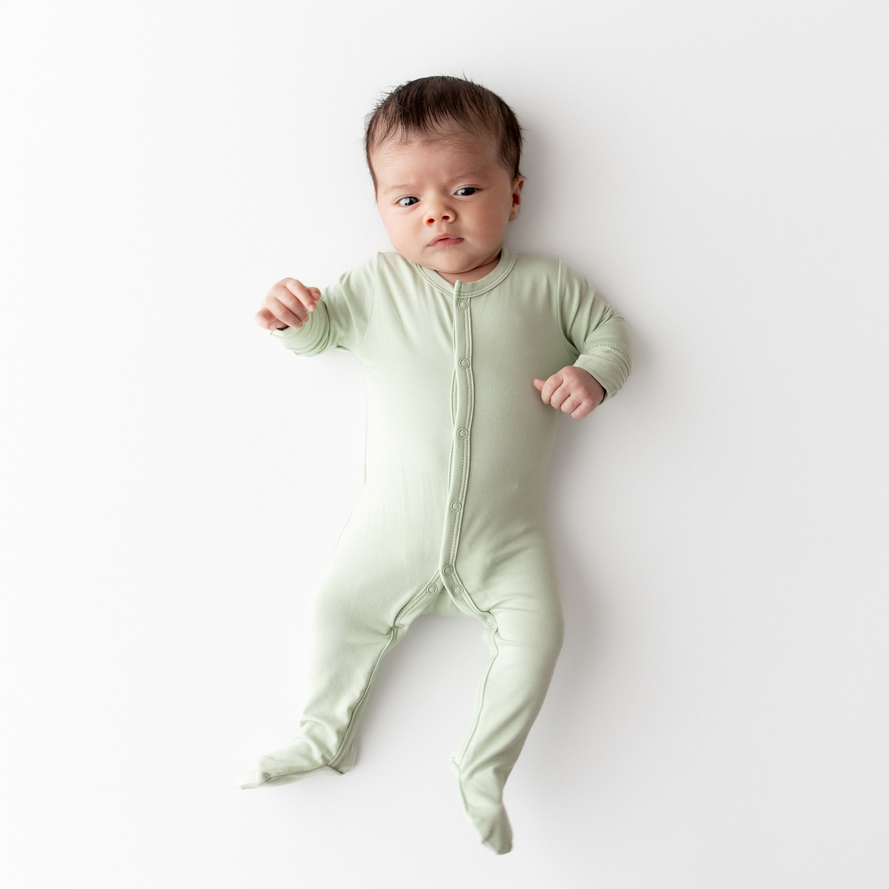 Baby wearing a light snap footed onesie on a white background