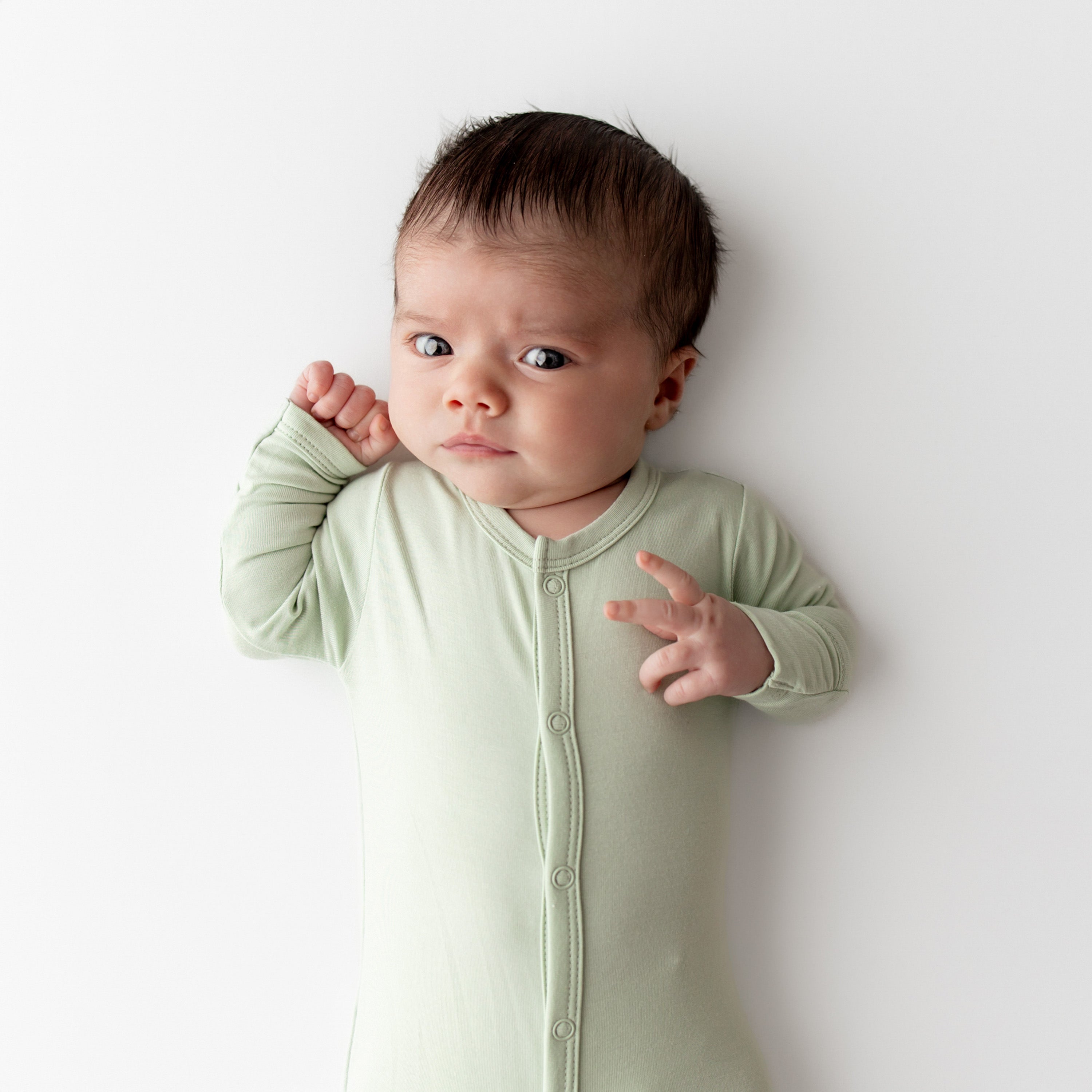 Baby wearing a light green footie against a white background