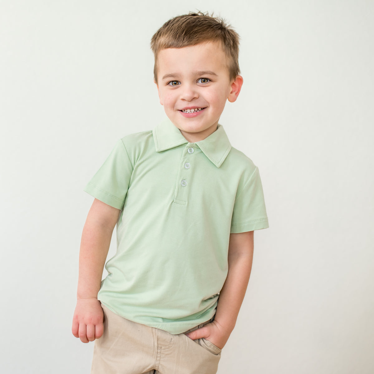 Young boy wearing a light green polo shirt against a plain background