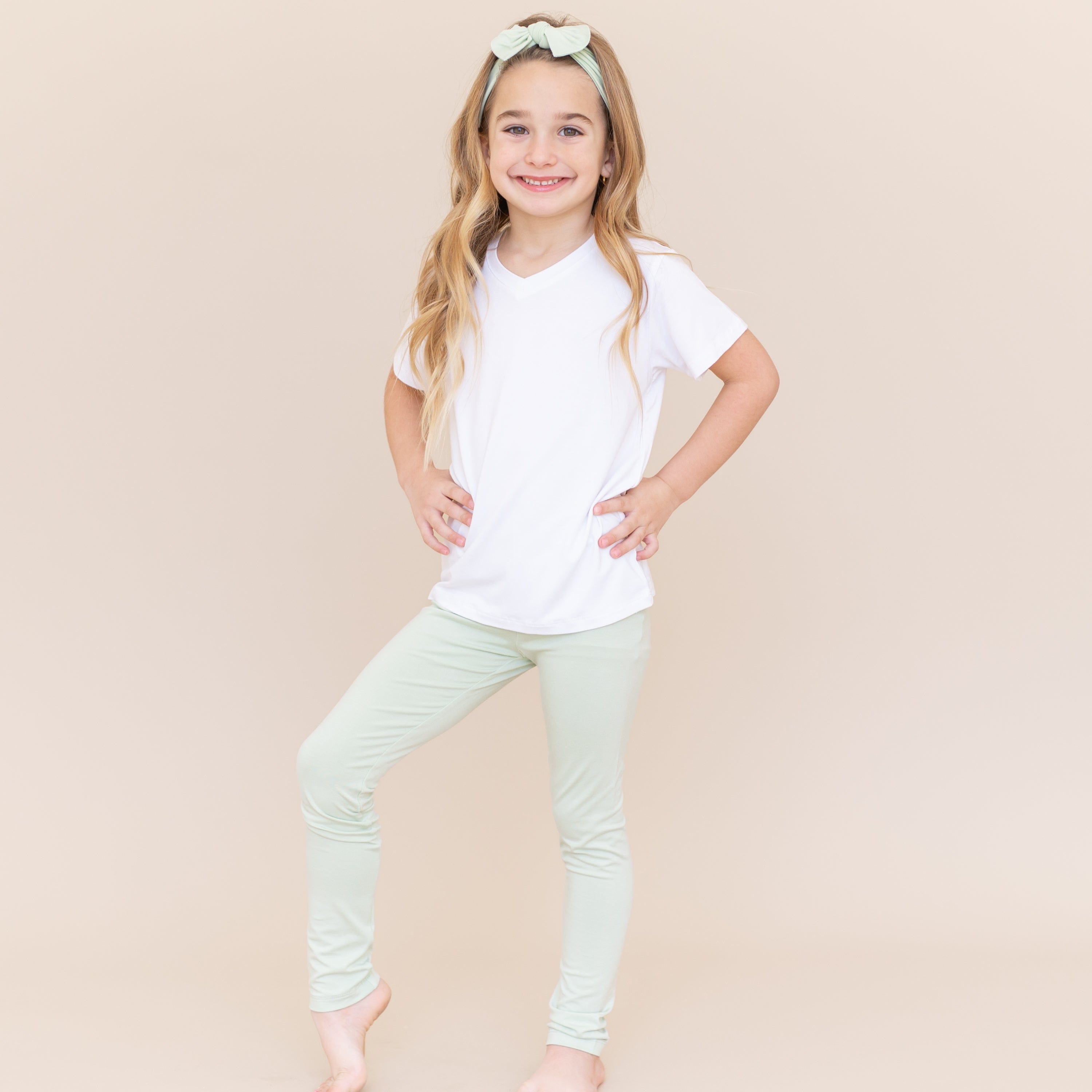 Young smiling girl wearing the Toddler Leggings in Basil and a white v-neck shirt