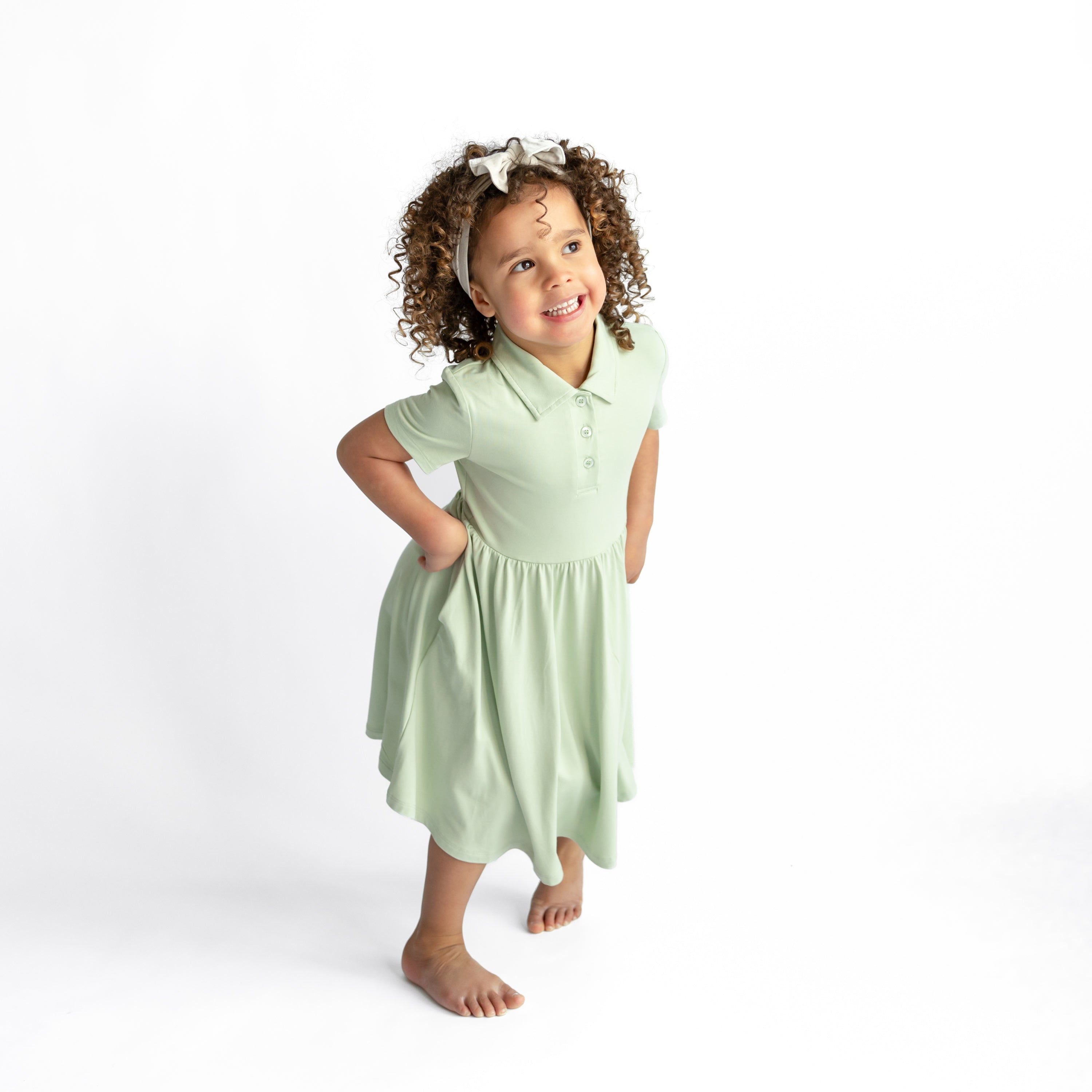 Smiling girl posing wearing the Polo Dress in Basil in front of a white background