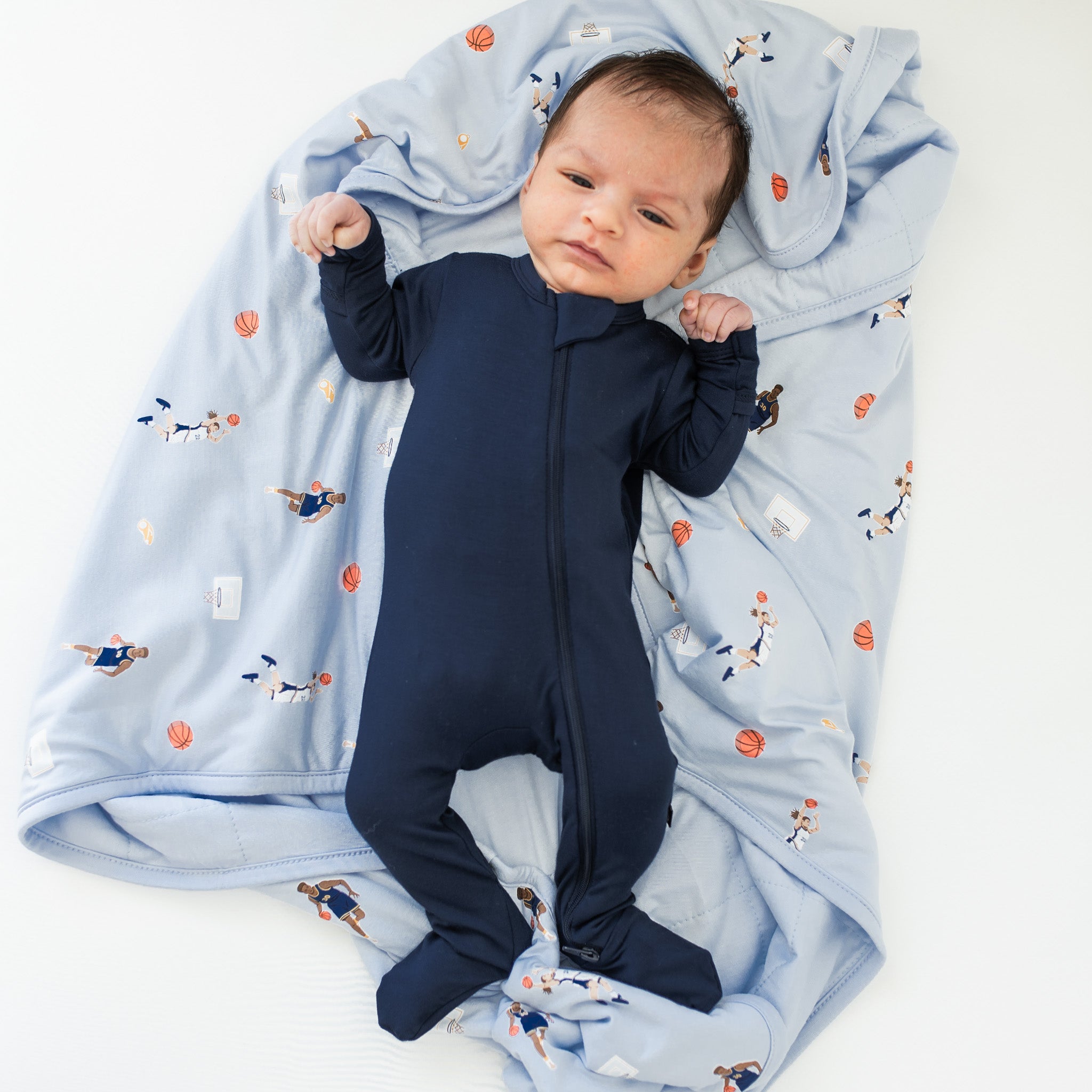 Infant laying on a Baby Blanket in Basketball wearing a Navy zippered footie