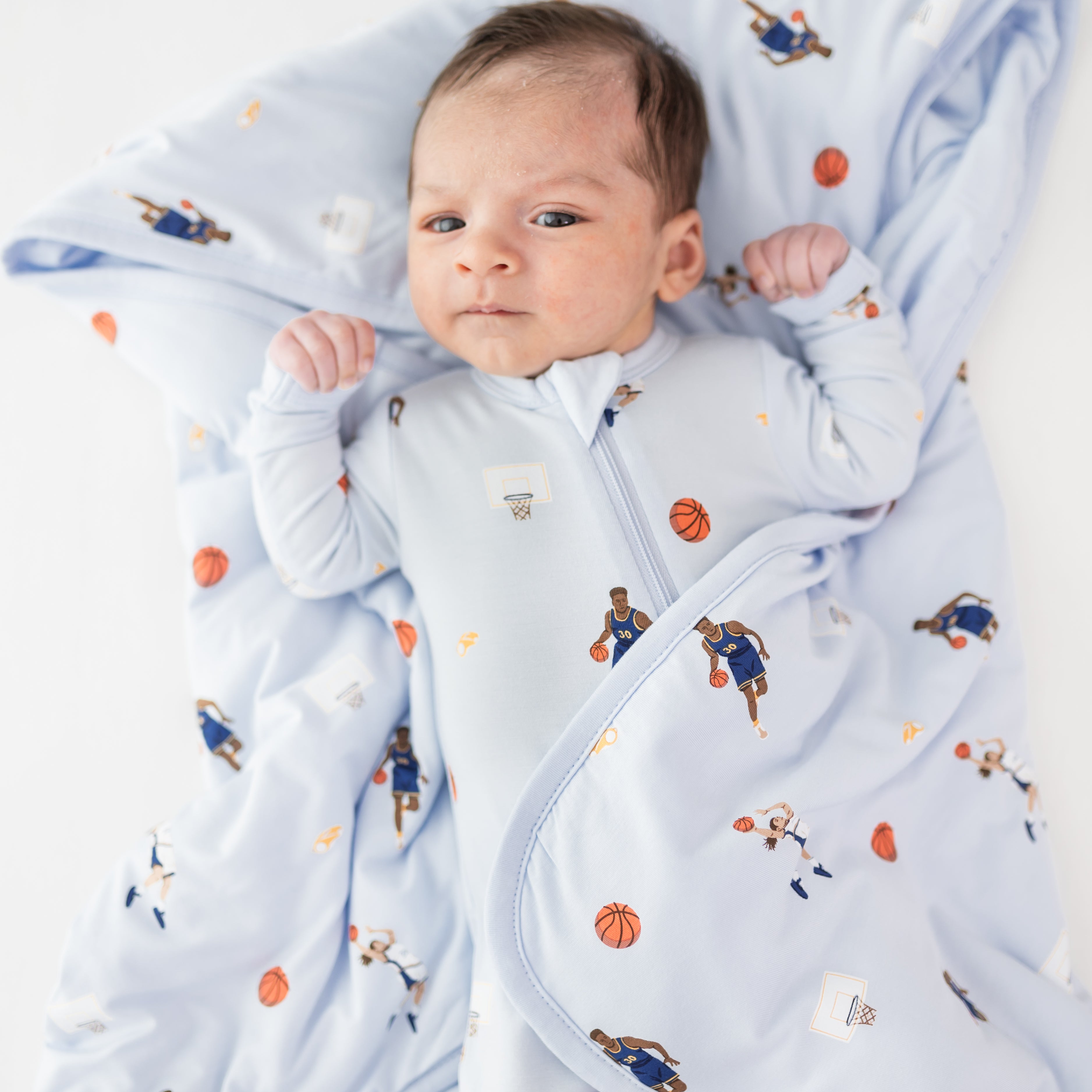 Close up of infant laying on a Baby Blanket in Basketball wearing a matching zippered romper