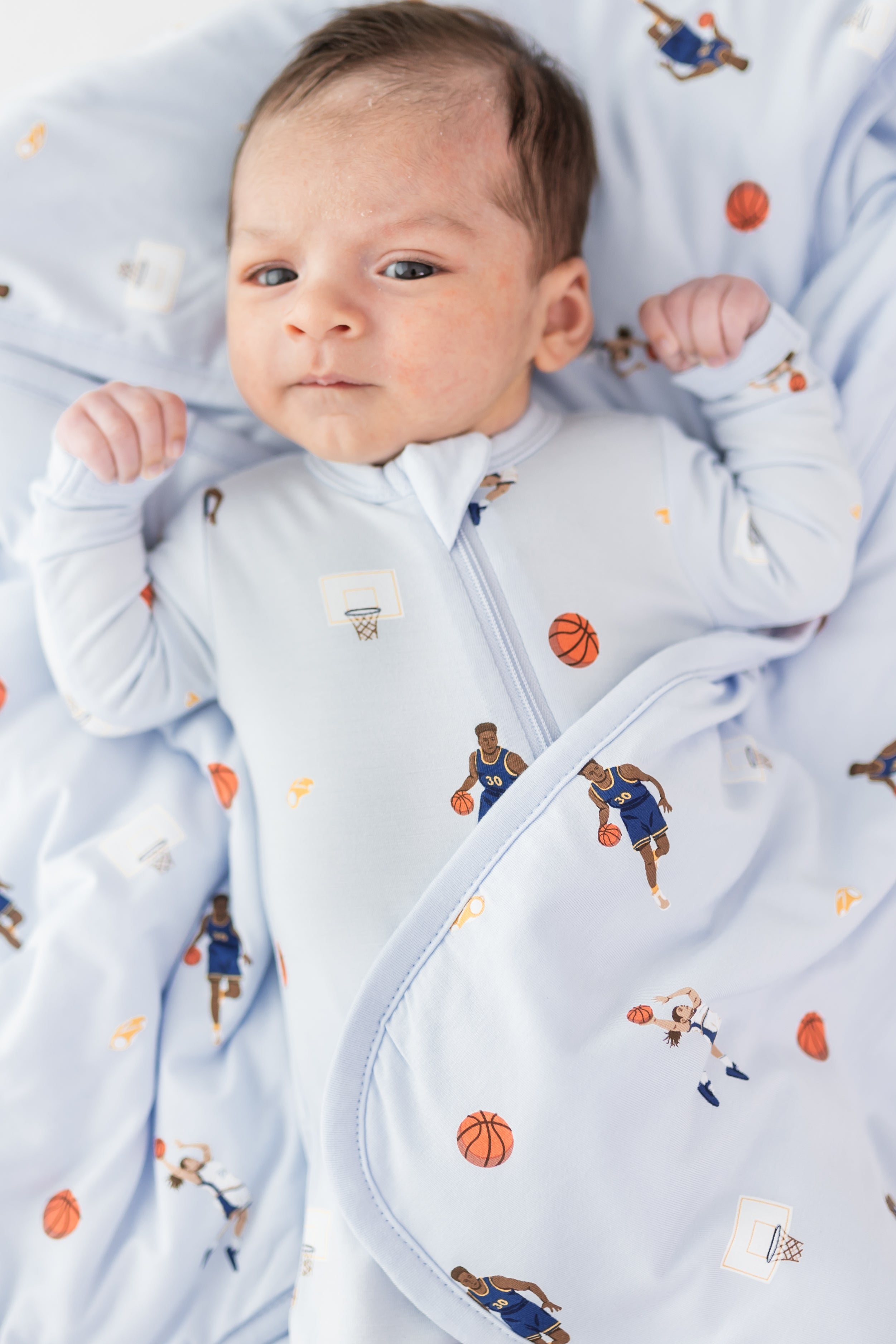 Close up of infant laying on a Baby Blanket in Basketball wearing a matching zippered romper