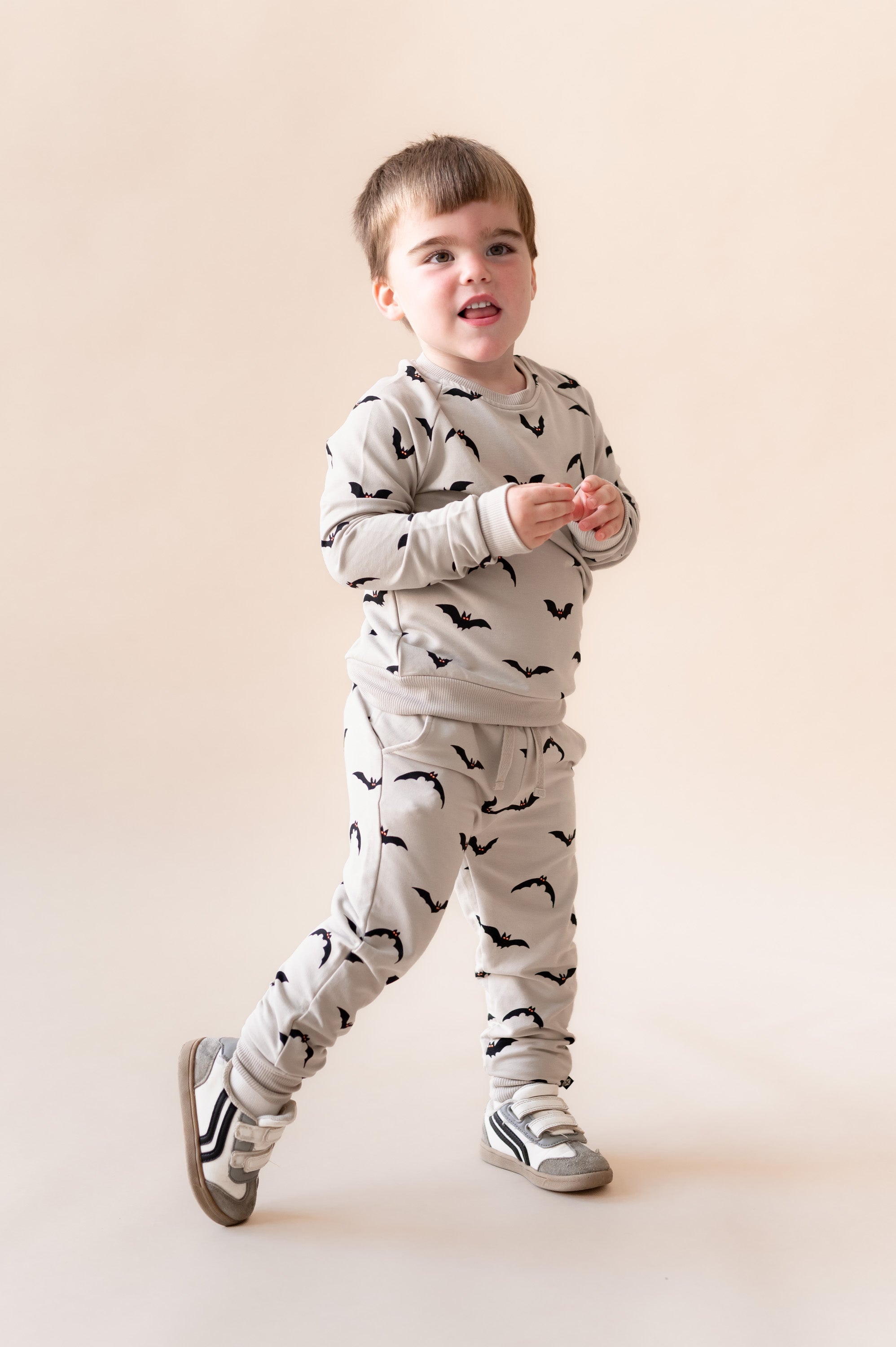 Boy posing in Long Sleeve Jogger Set in Bats print and shoes on a beige background