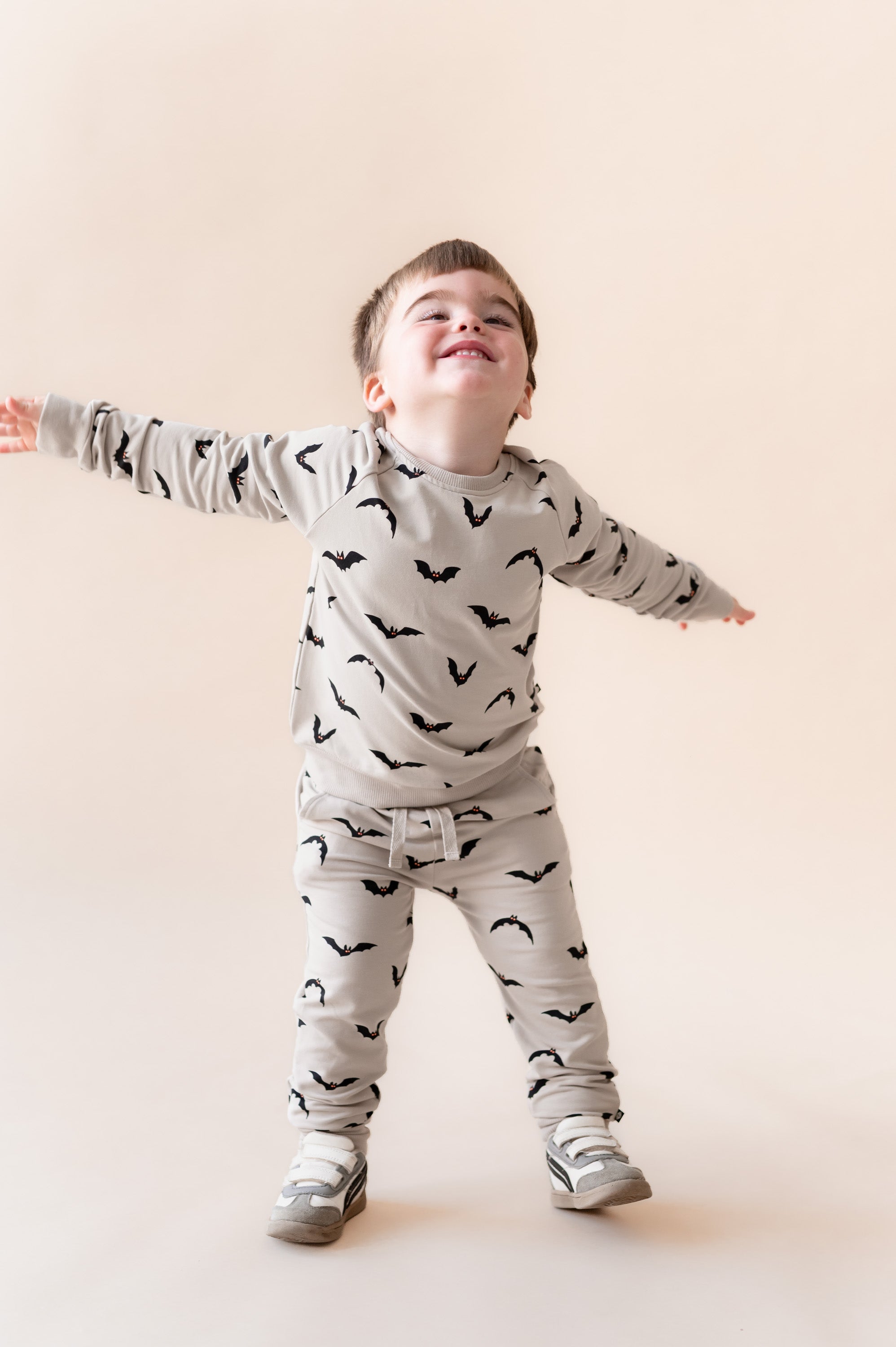 Boy in Long Sleeve Jogger Set in Bats print and shoes on a beige background
