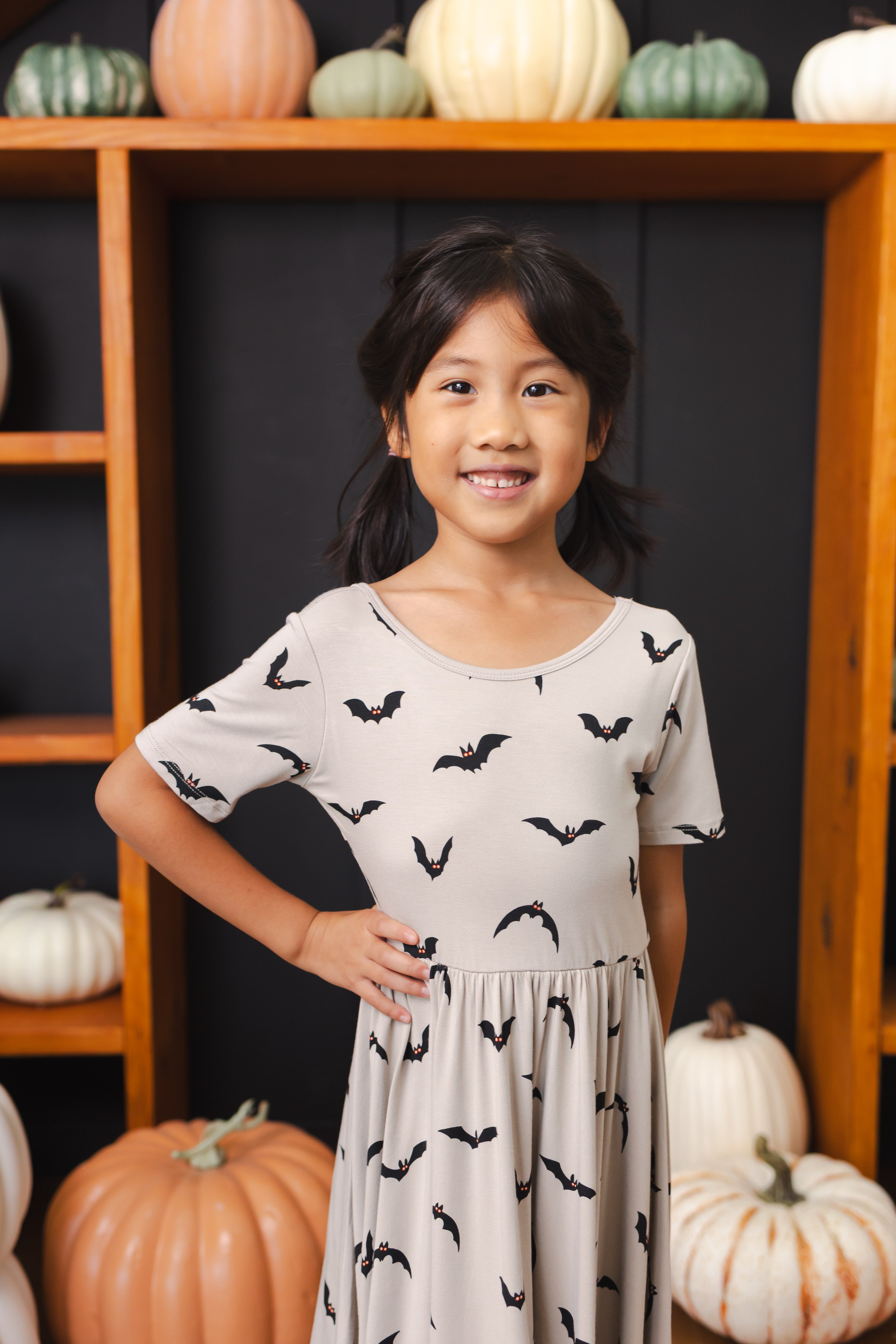 Close up of Girl wearing Twirl Dress in Bats print smiling in front of pumpkin decorations
