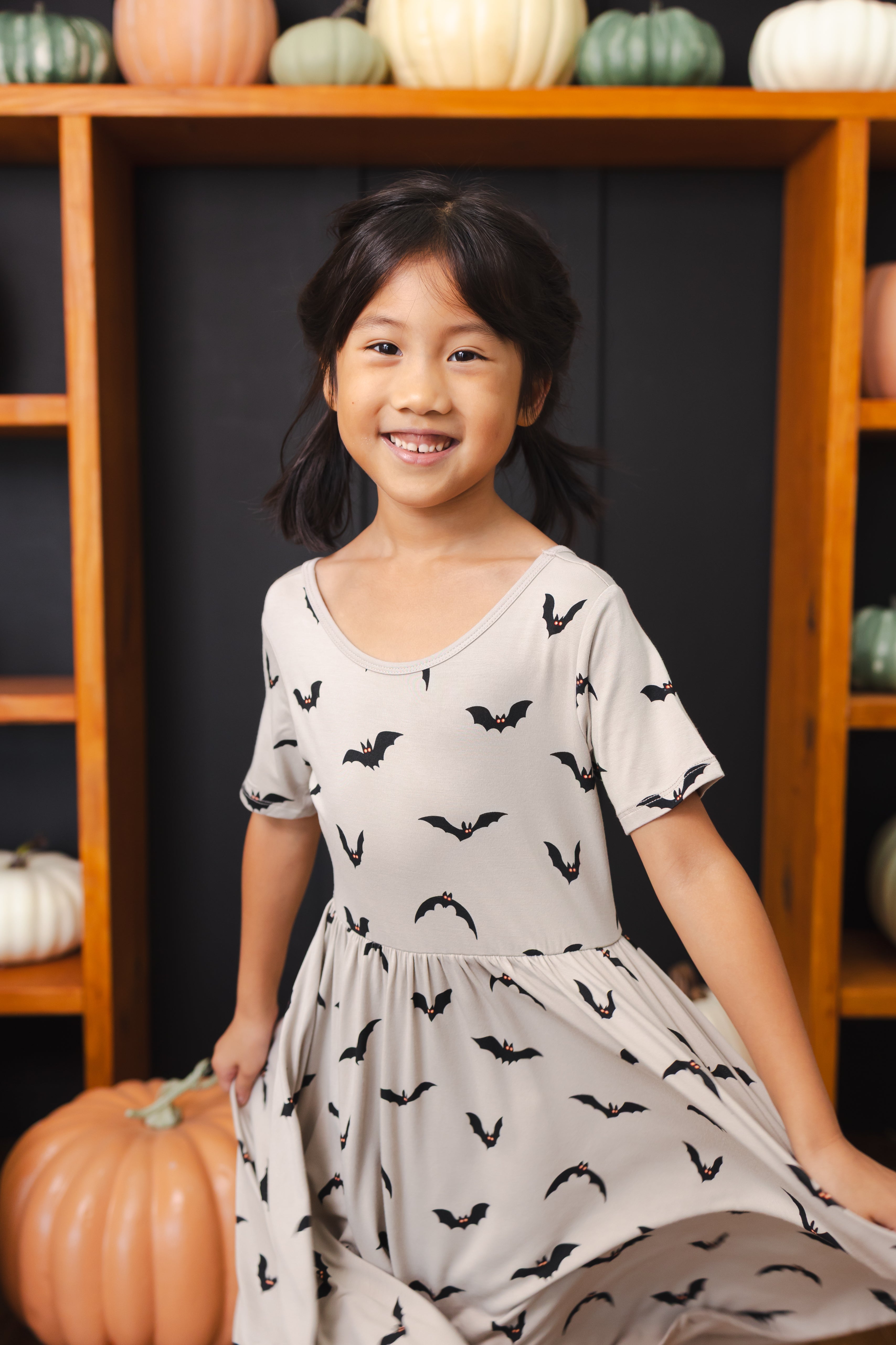 Girl wearing Twirl Dress in Bats print smiling in front of pumpkin decorations