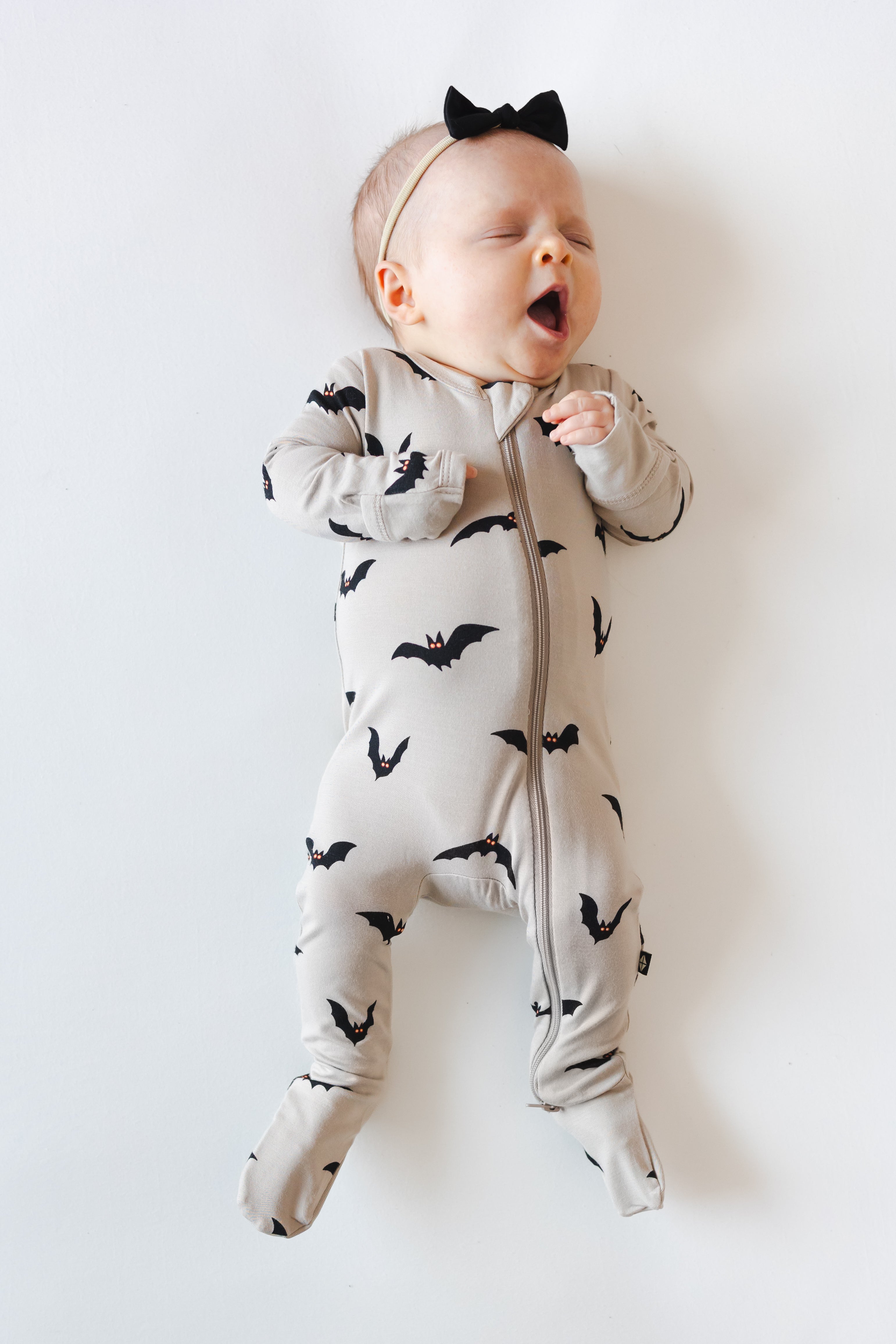 Baby yawning in Zippered Footie in Bats print and a bow on a white background