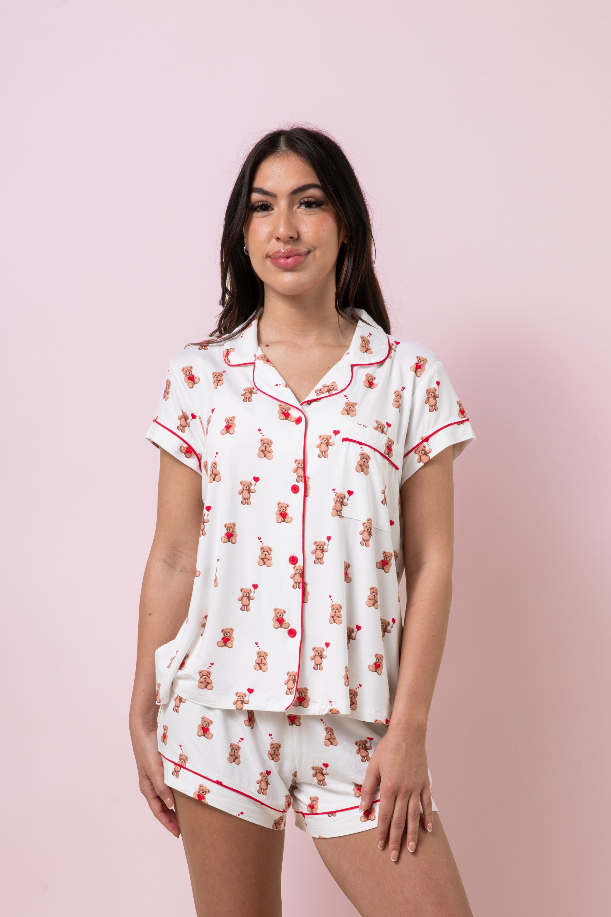 Female model standing in front of a pink background wearing the soft and breathable Women's Short Sleeve Pajama Set in Bear Hearts