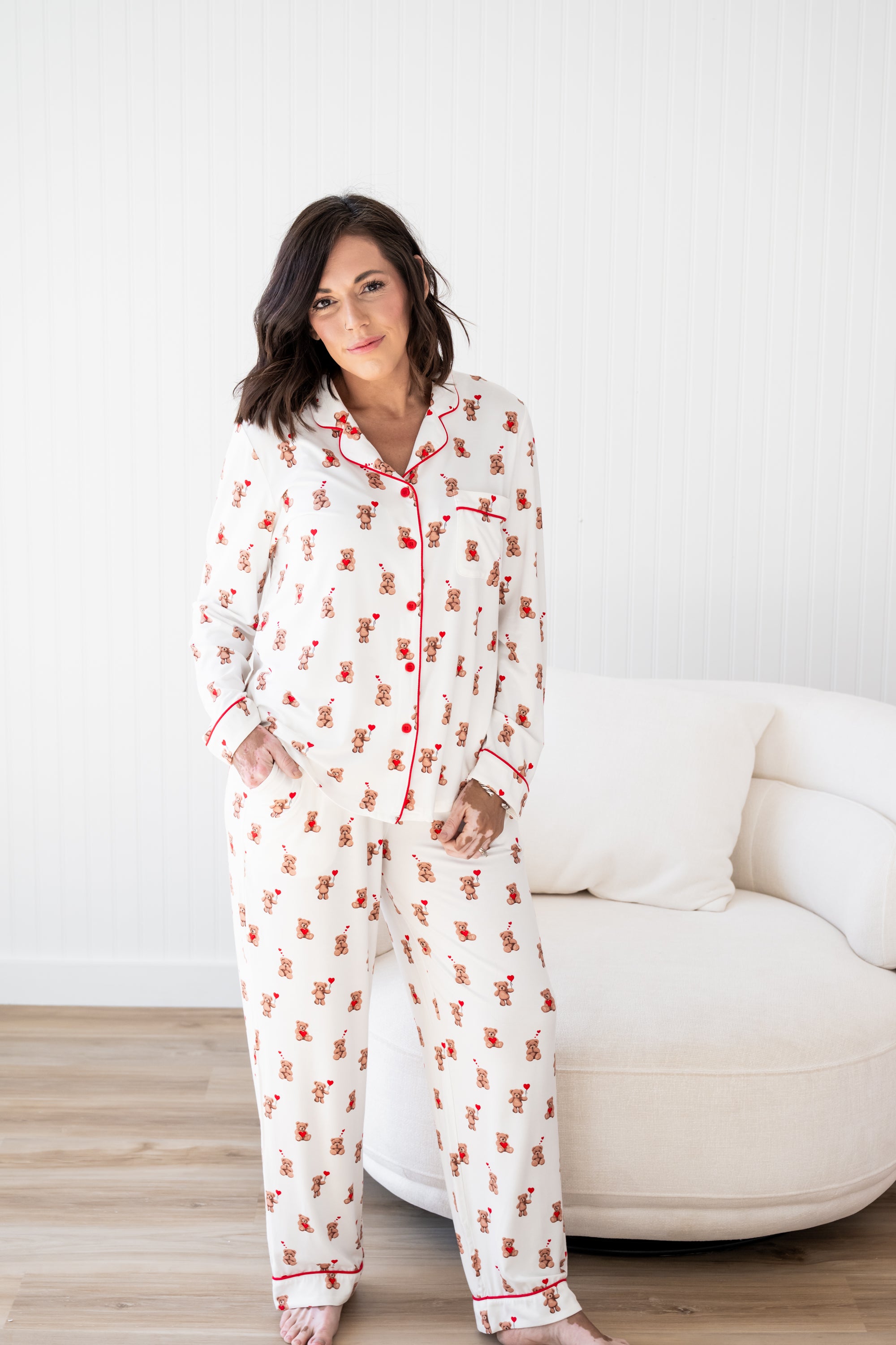 Female model posing in front of a cream sofa chair wearing the Long-Sleeved Women's Pajama Set in Bear Hearts