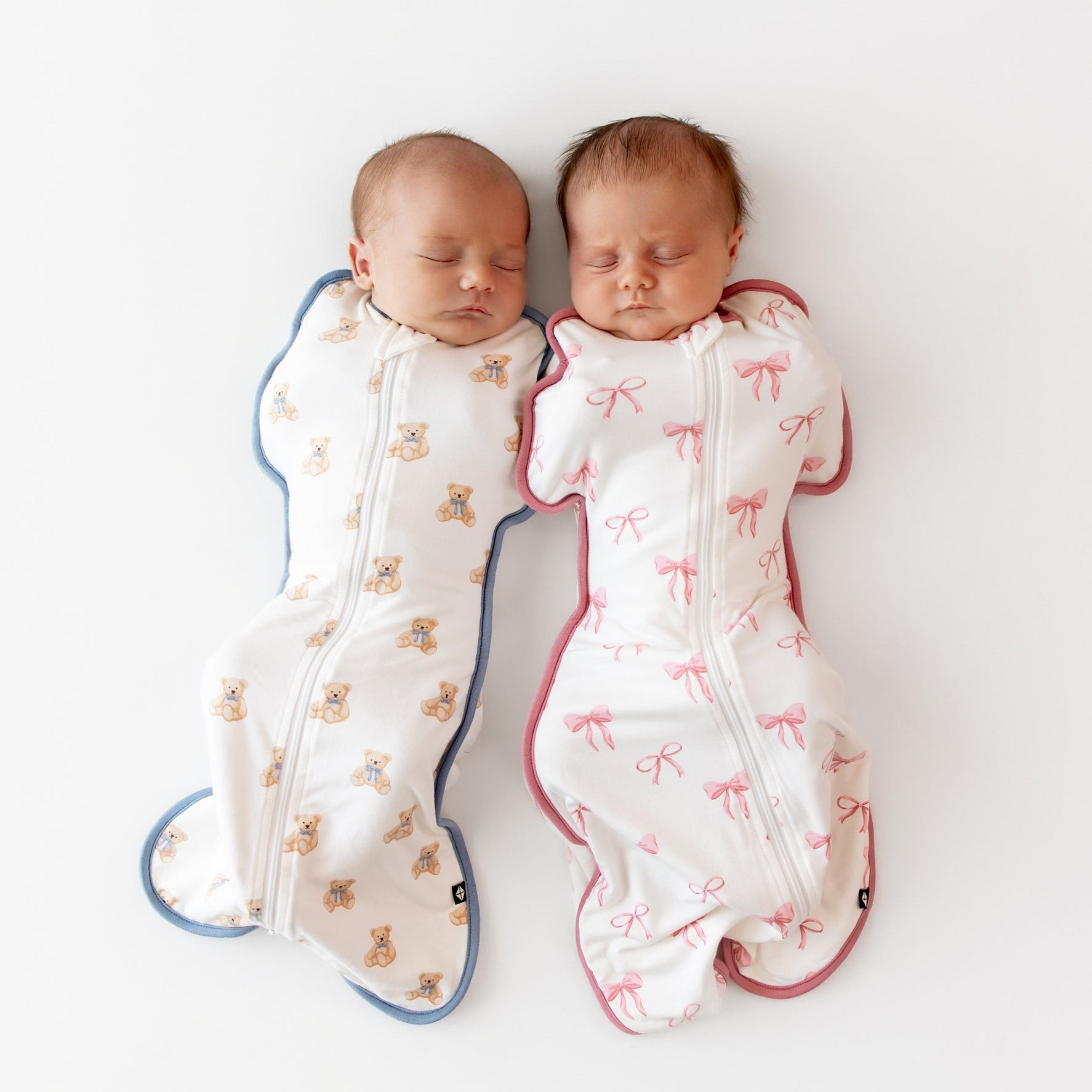 Two babies wrapped in patterned swaddles on a white background