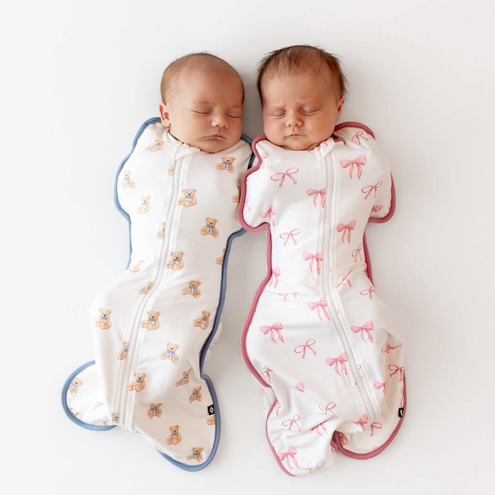 Two babies wrapped in patterned swaddles on a white background