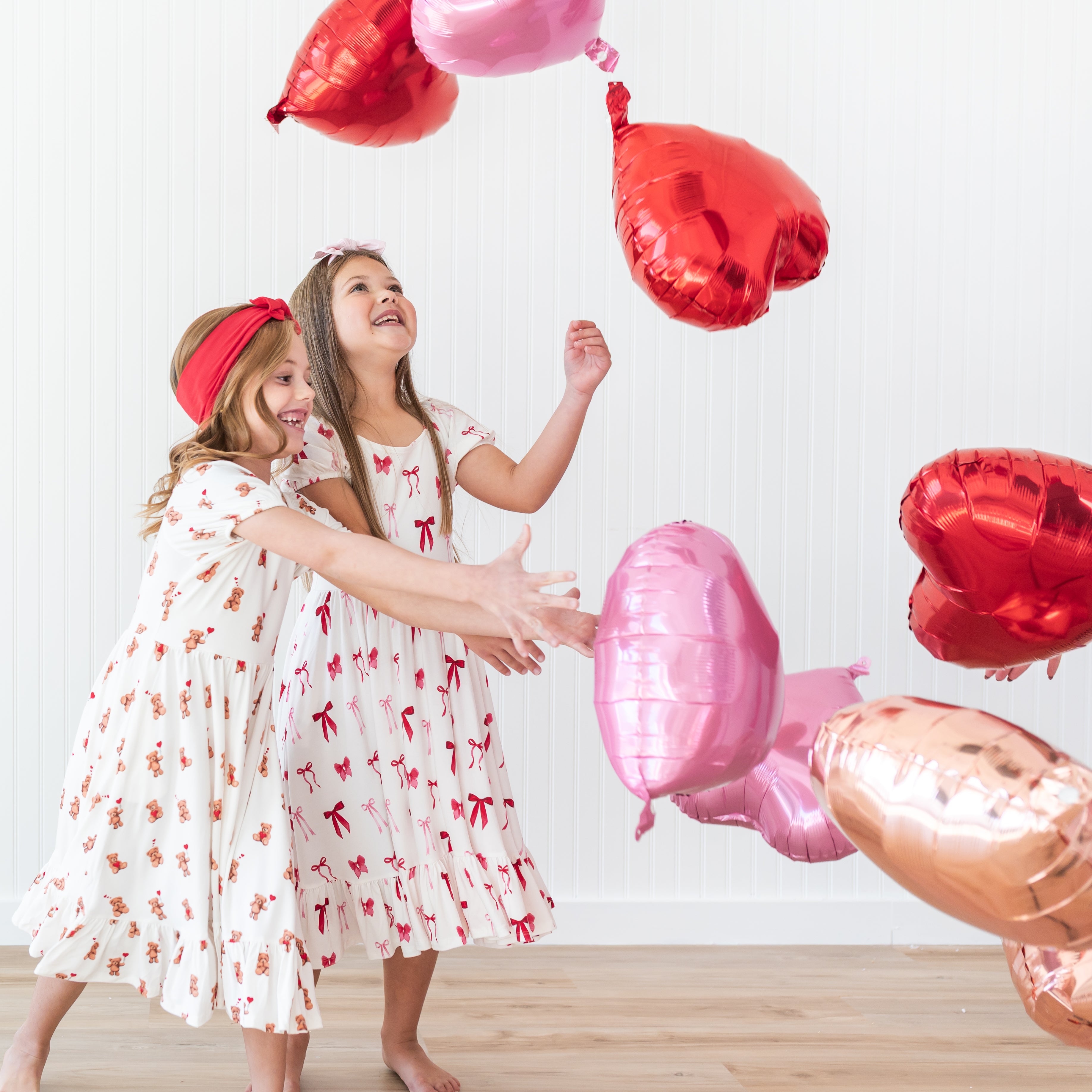 Two girls playing with helium heart balloons wearing the Puff Sleeve Twirl Dress in Small Love Bow and Bear Hearts