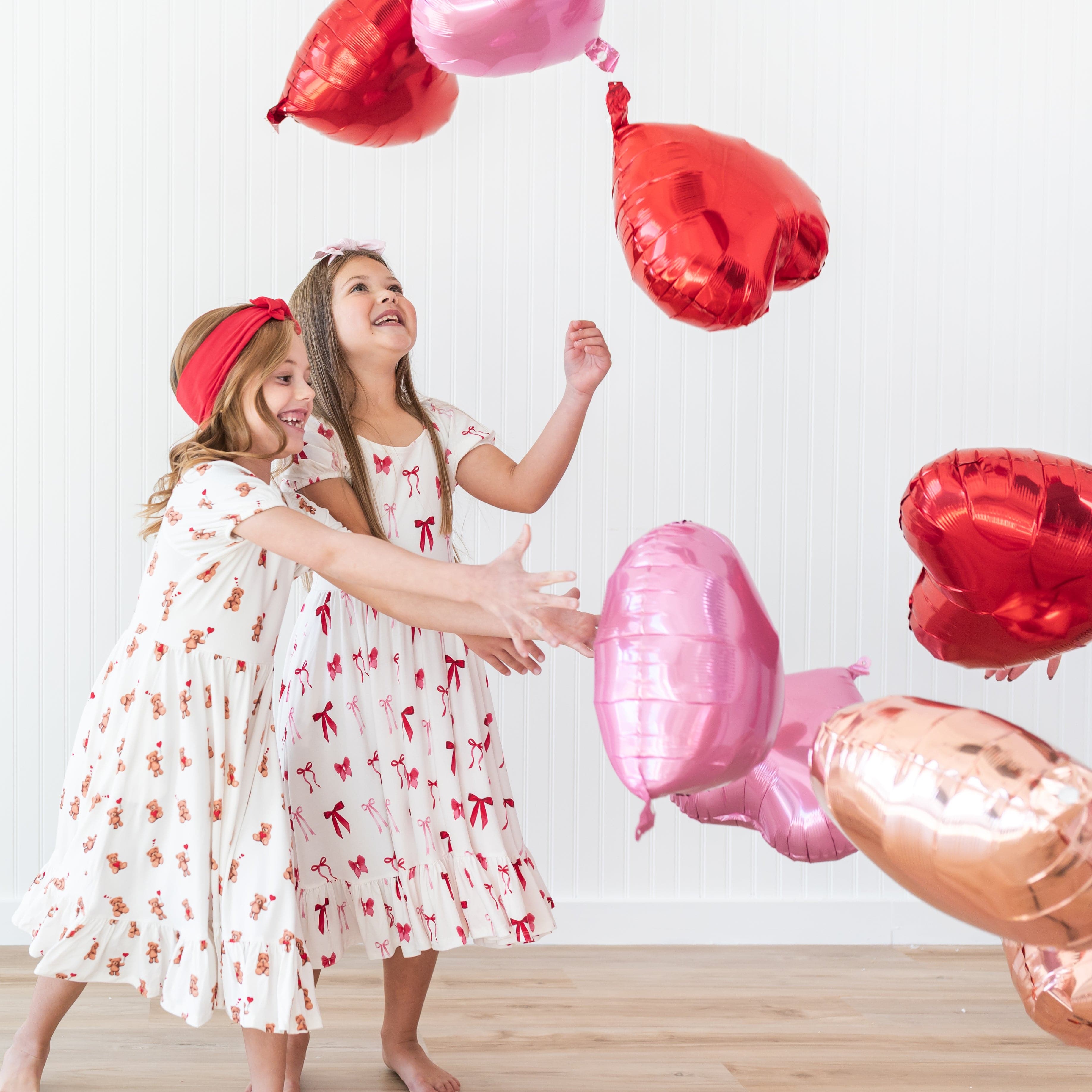 Two girls playing with helium heart balloons wearing the Puff Sleeve Twirl Dress in Small Love Bow and Bear Hearts