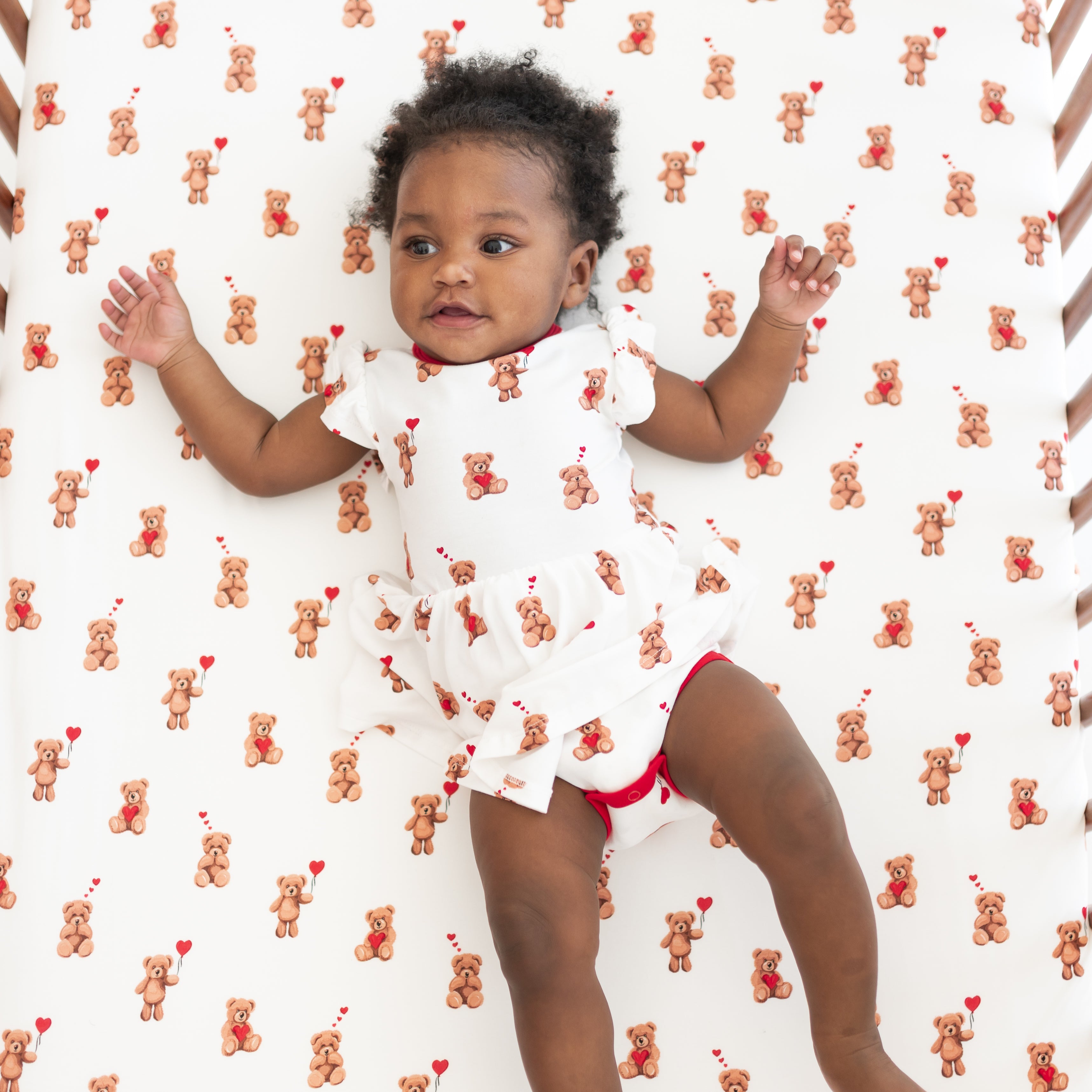 Young toddler girl laying in a crib on the Crib Sheet in Bear Hearts wearing a matching twirl bodysuit dress