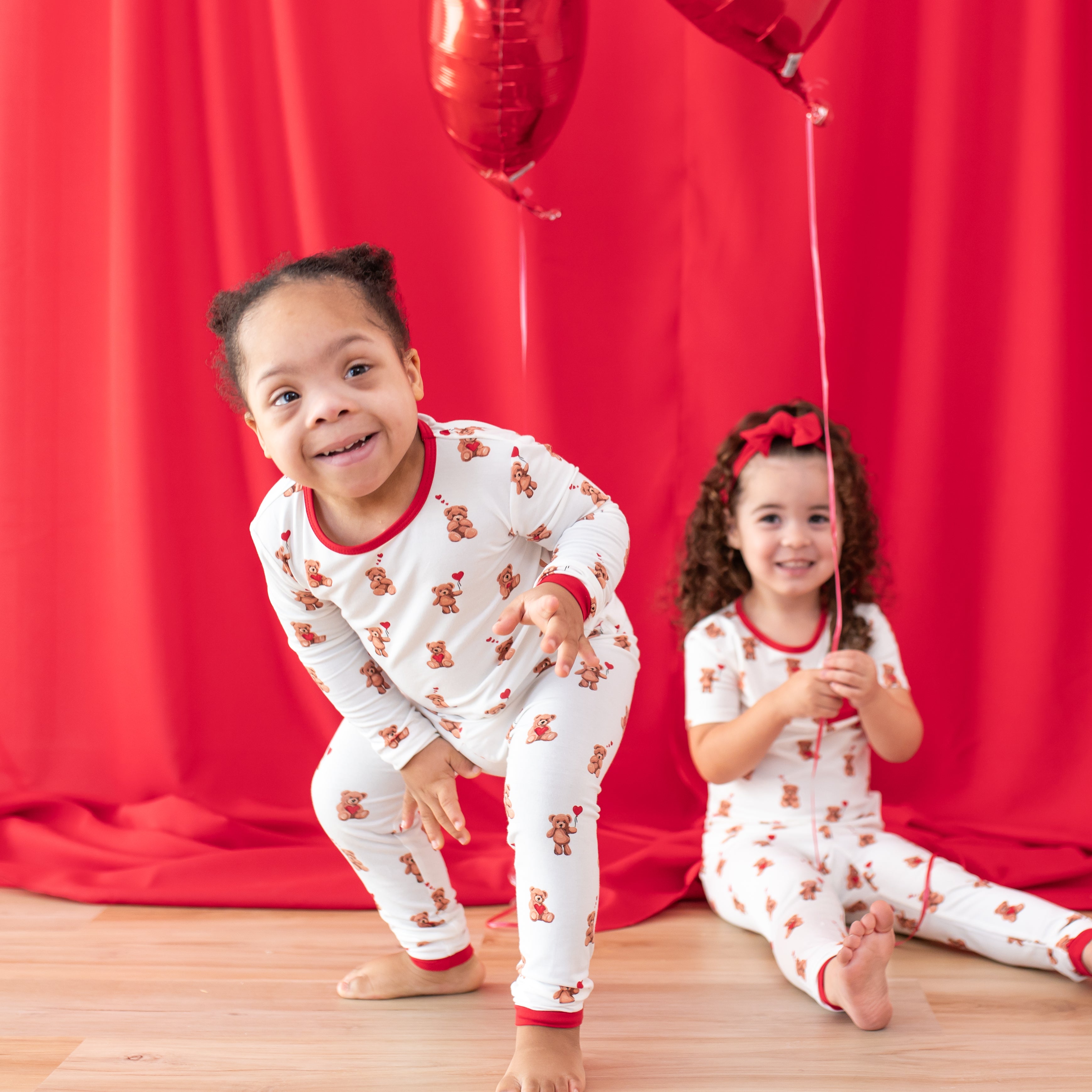 Two young children in front of a red curtain wearing toddler pajamas from the Bear Hearts collections