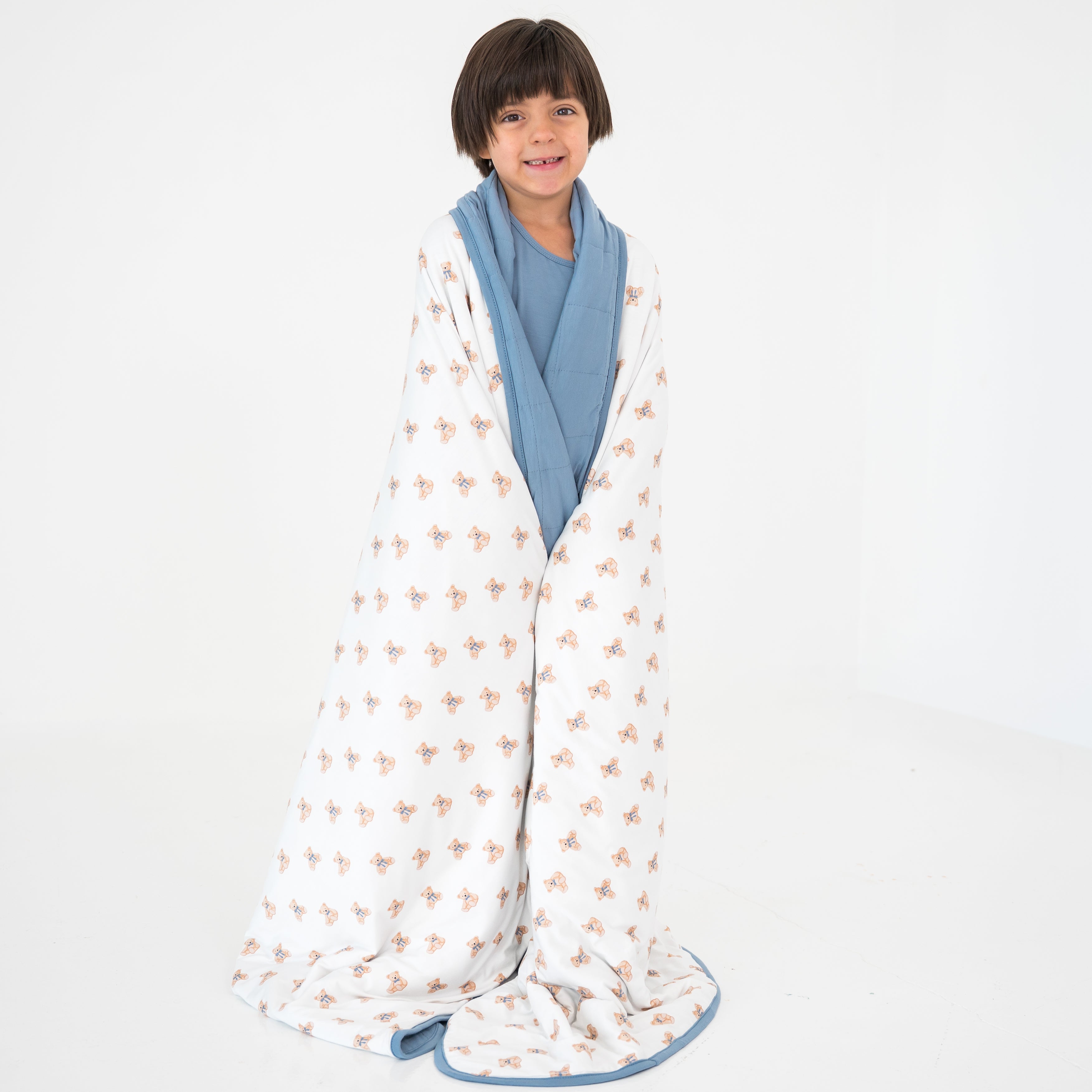 Child wrapped in a teddy bear patterned blanket with a plain background