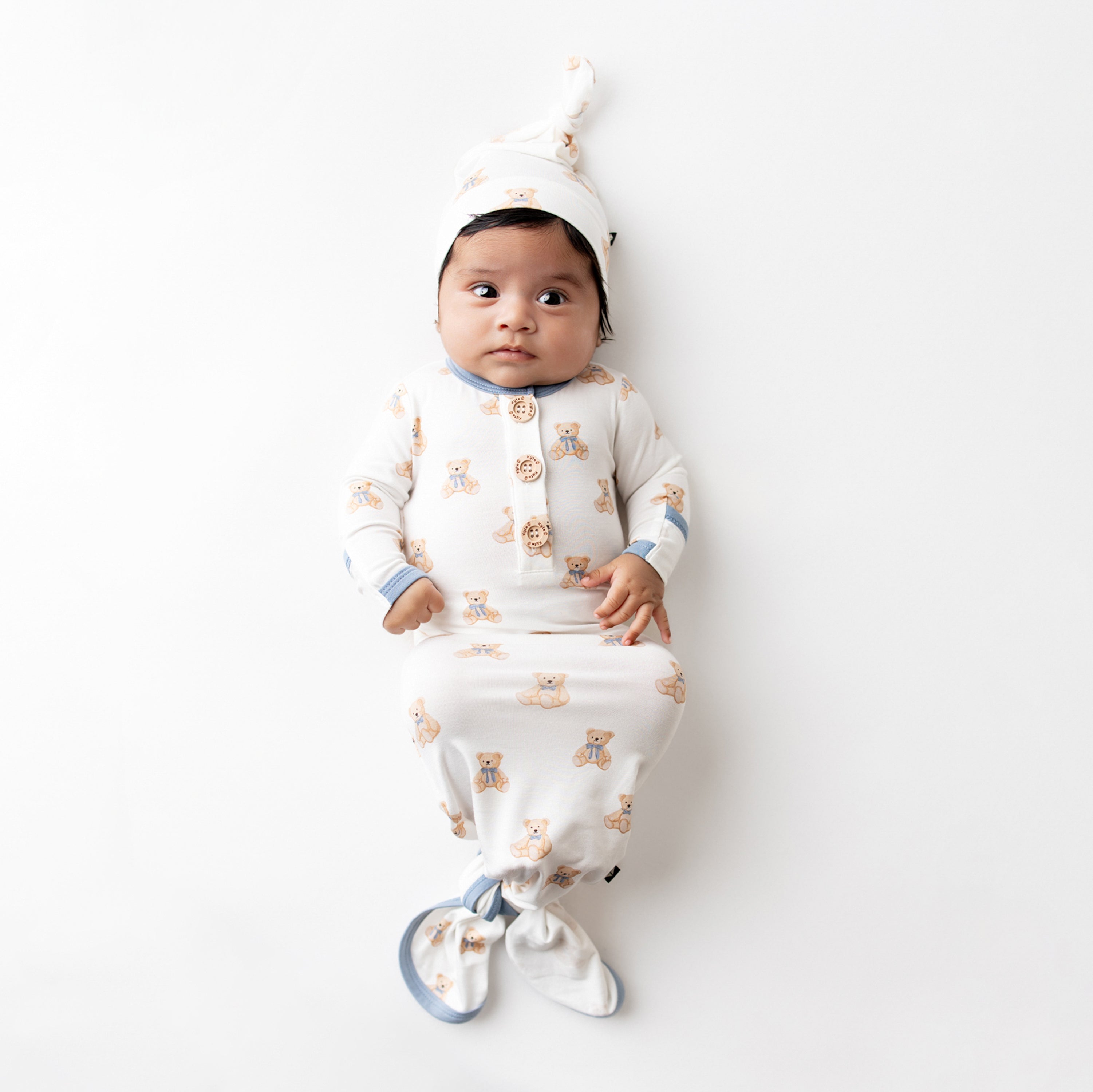 Infant laying on a flat white surface wearing the Knotted Gown with Hat Set in Teddy Bear