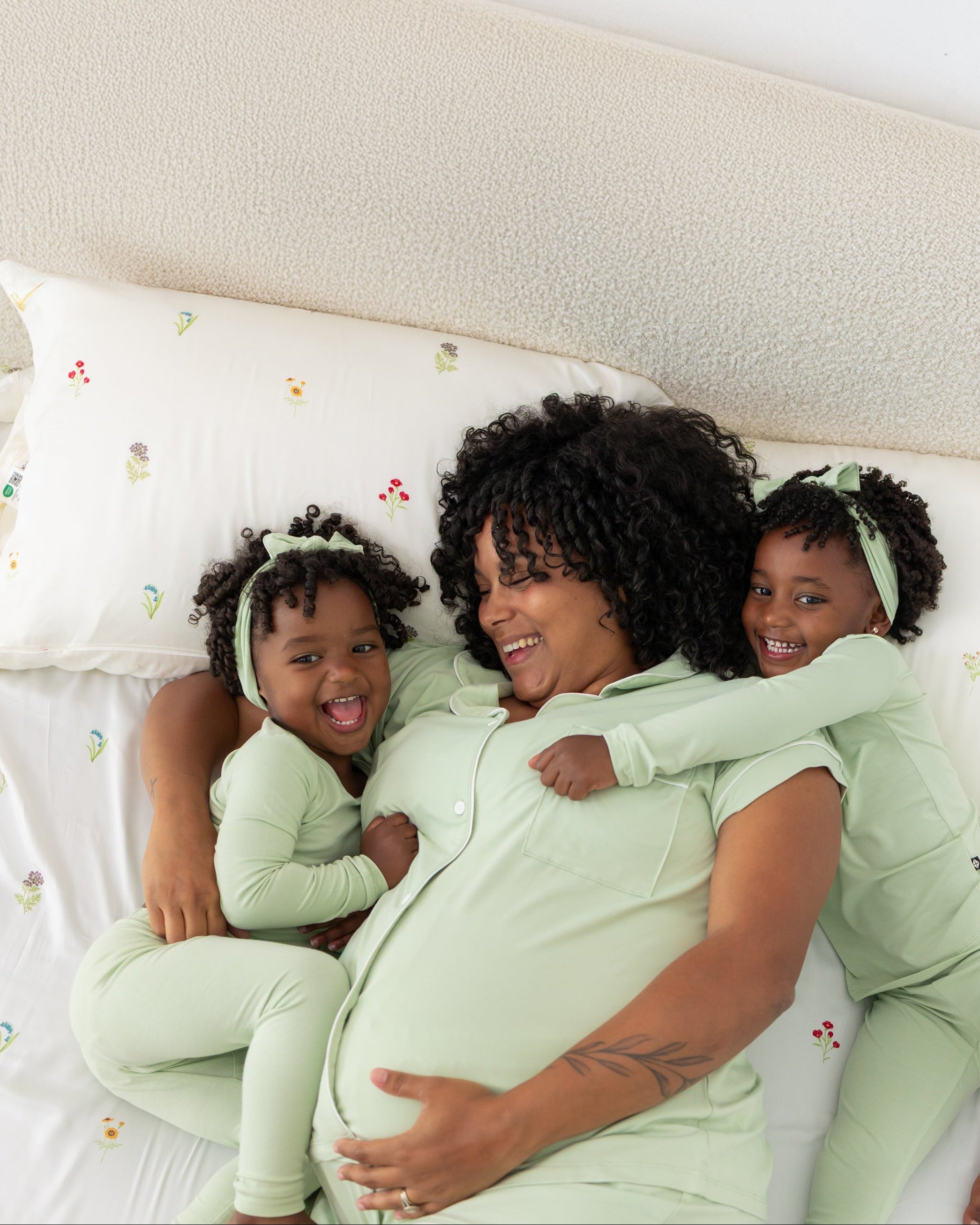 Woman lying on a bed with two children in matching green outfits, all smiling.
