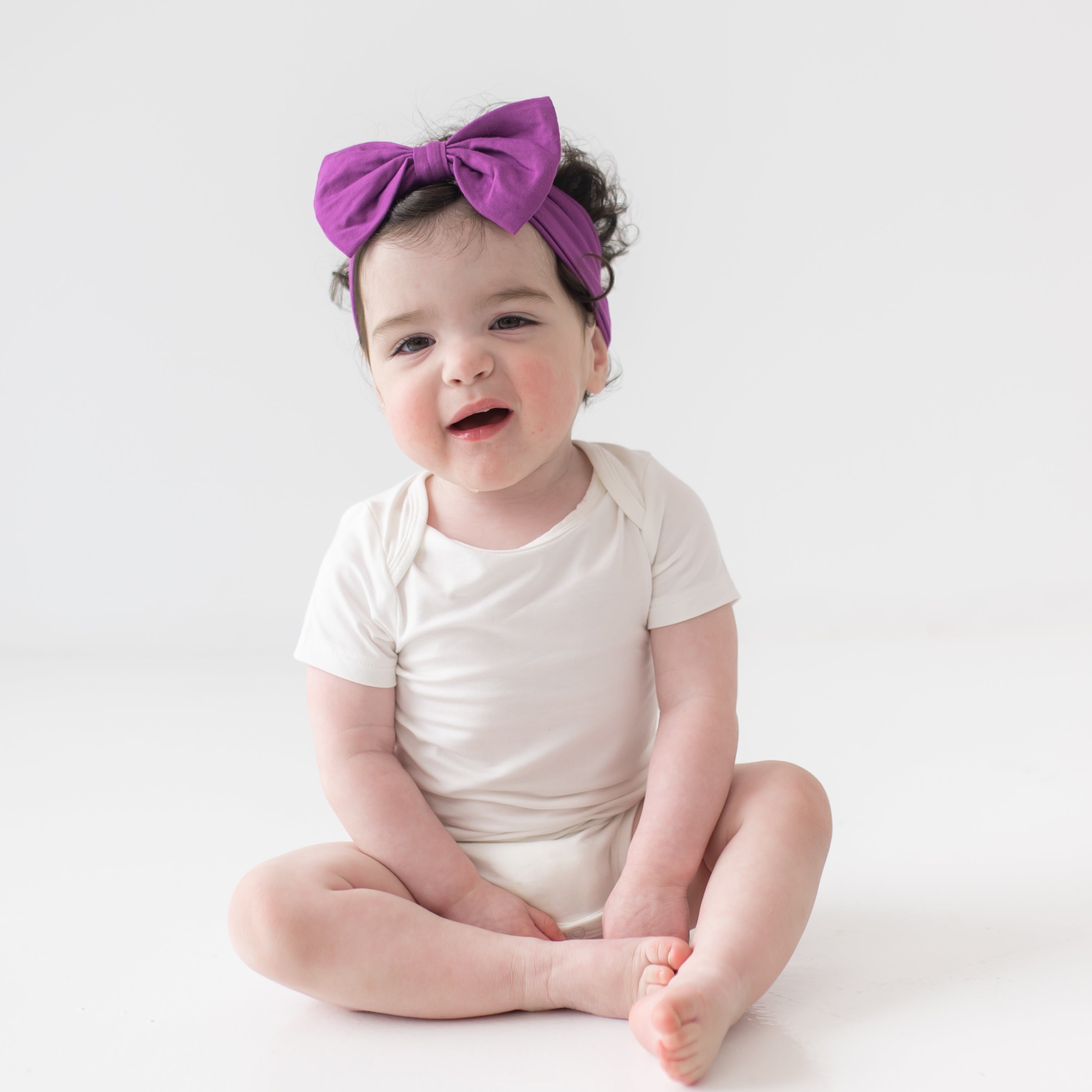 Baby sitting wearing cloud bodysuit and Bow Headband in Berry