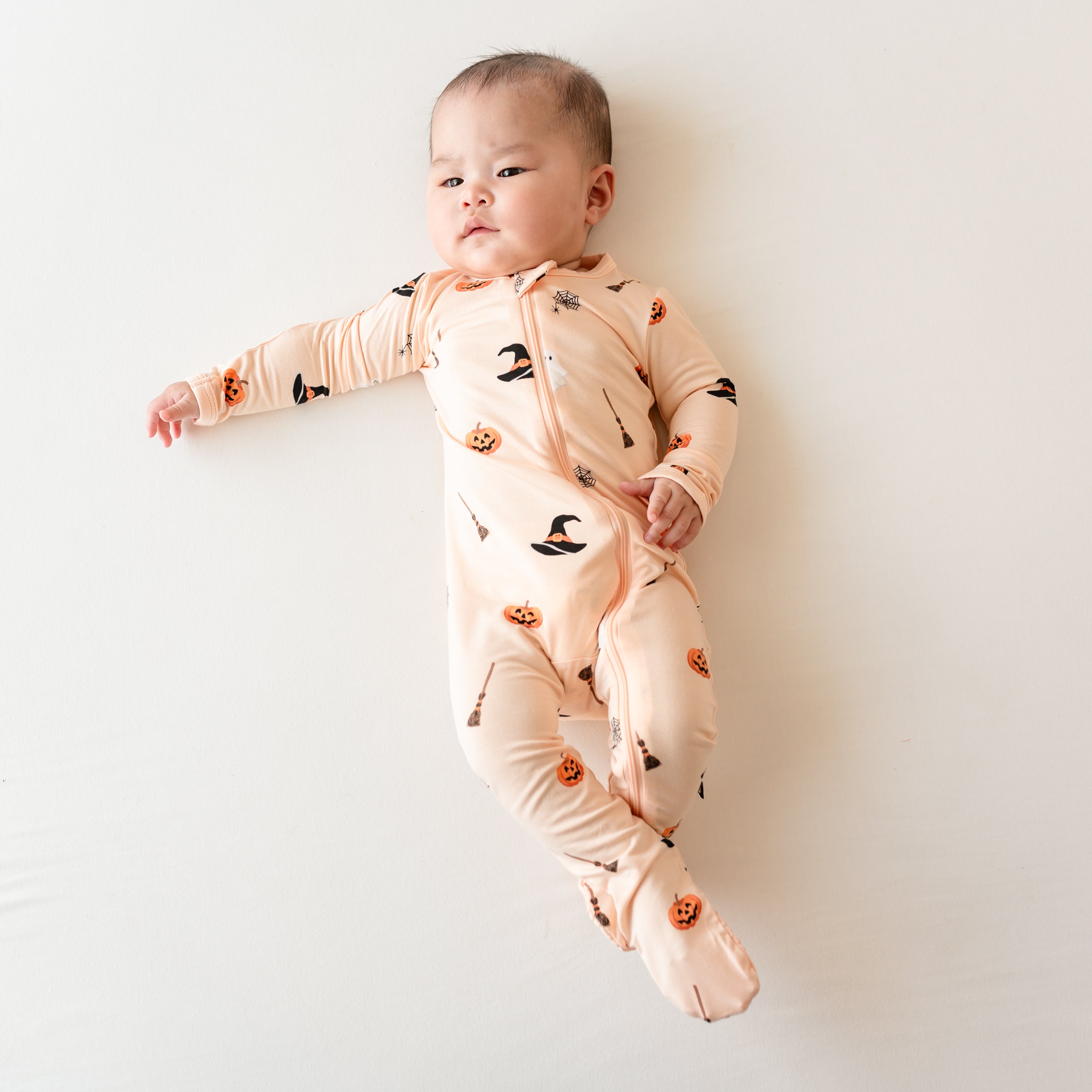 Infant laying with their arm out on a light neutral background wearing the Zippered Footie in Bewitched