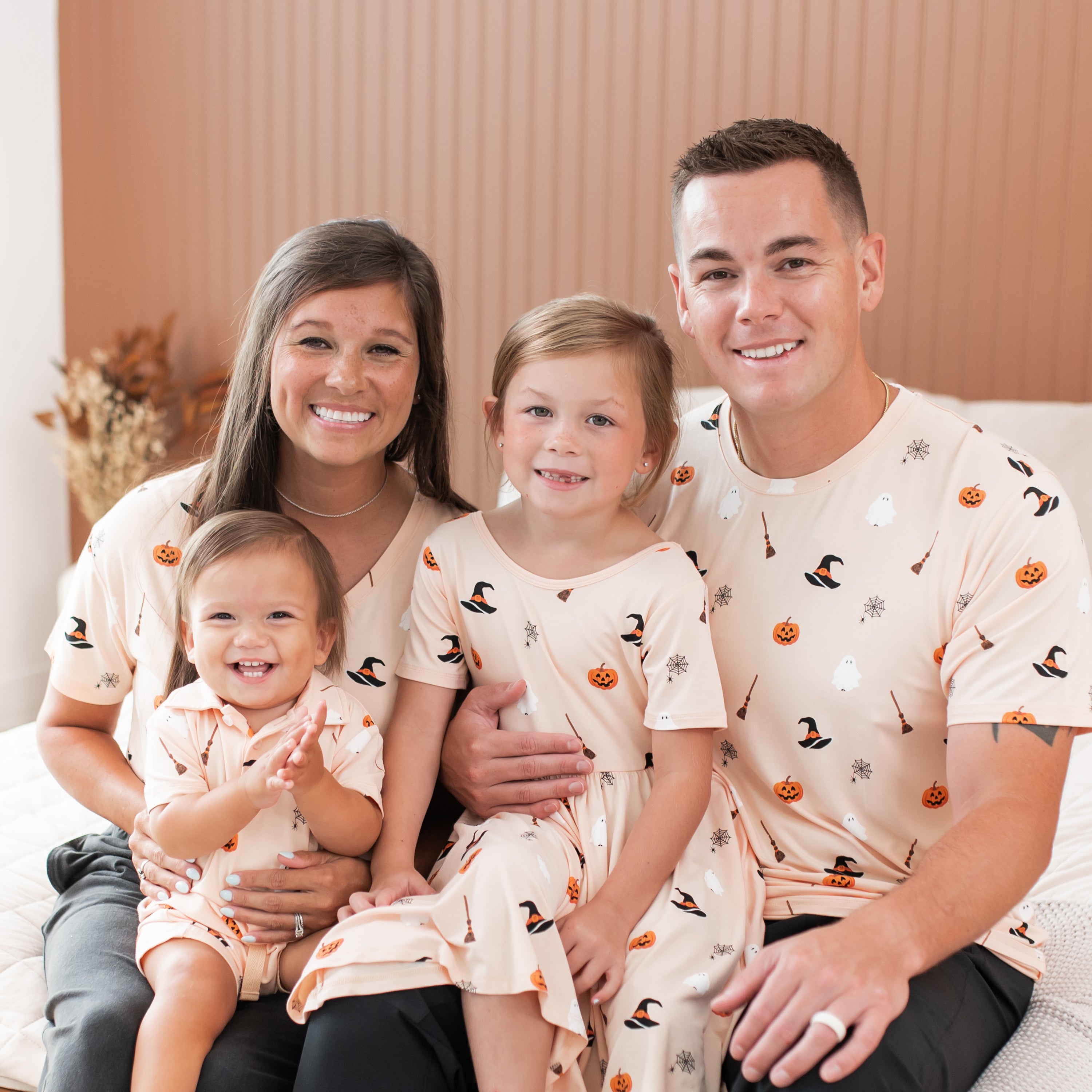 Family of four wearing matching Halloween-themed apparel sitting together.