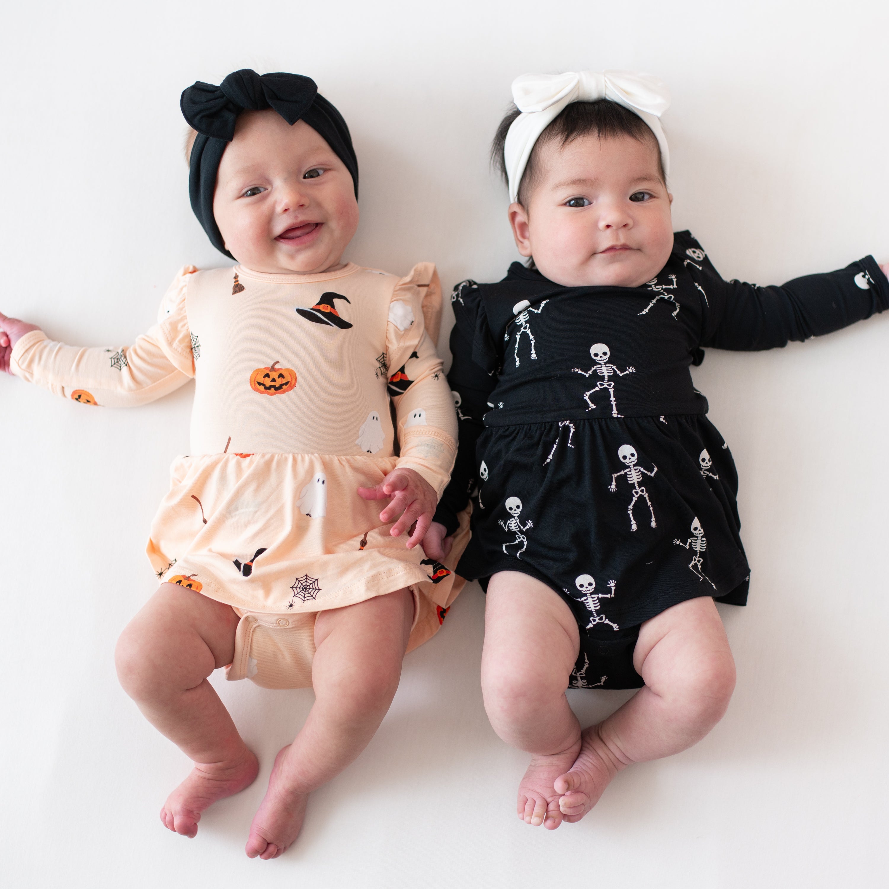 Two babies wearing Halloween-themed dresses on a white background