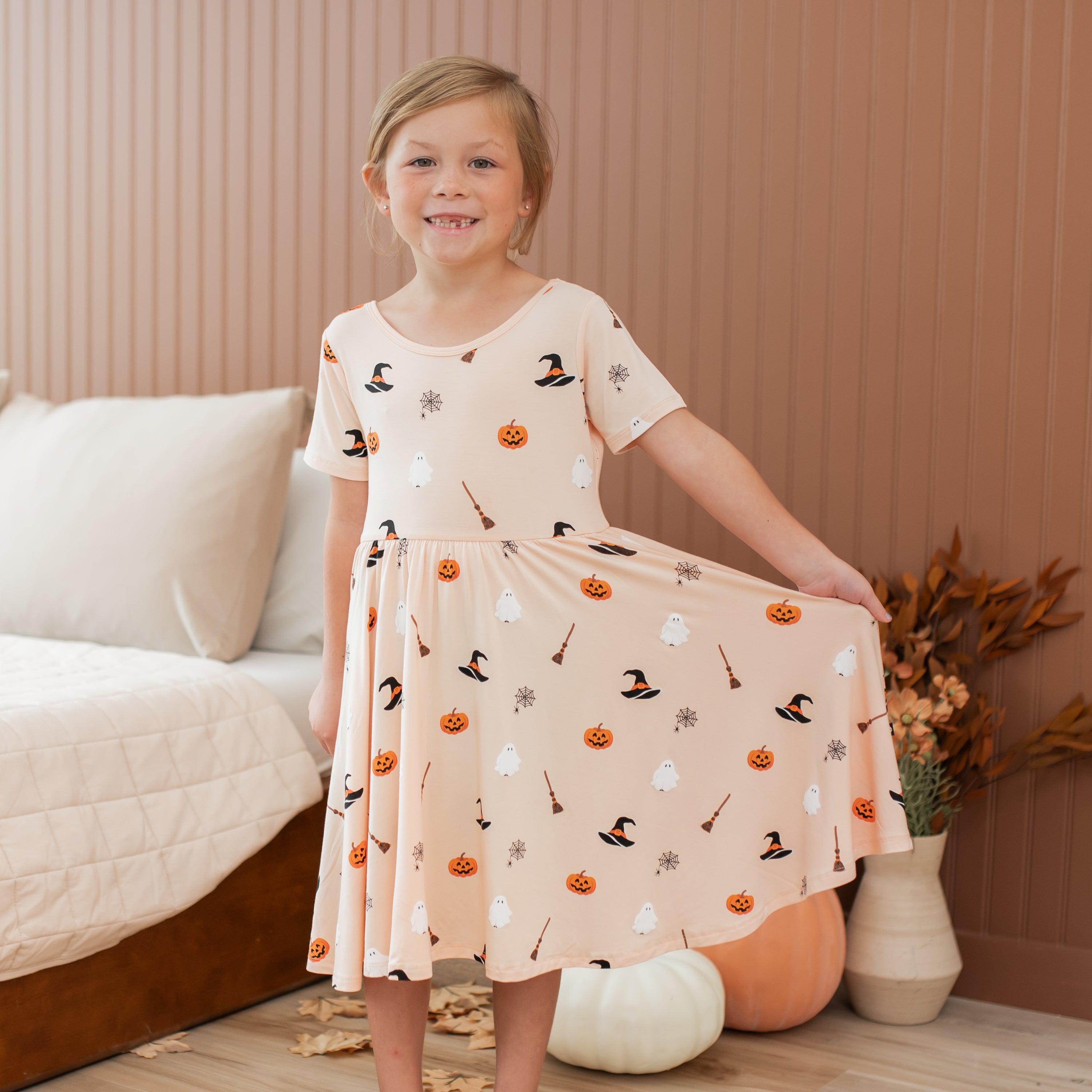 Young girl wearing a Halloween-themed peach colored dress in a cozy room.