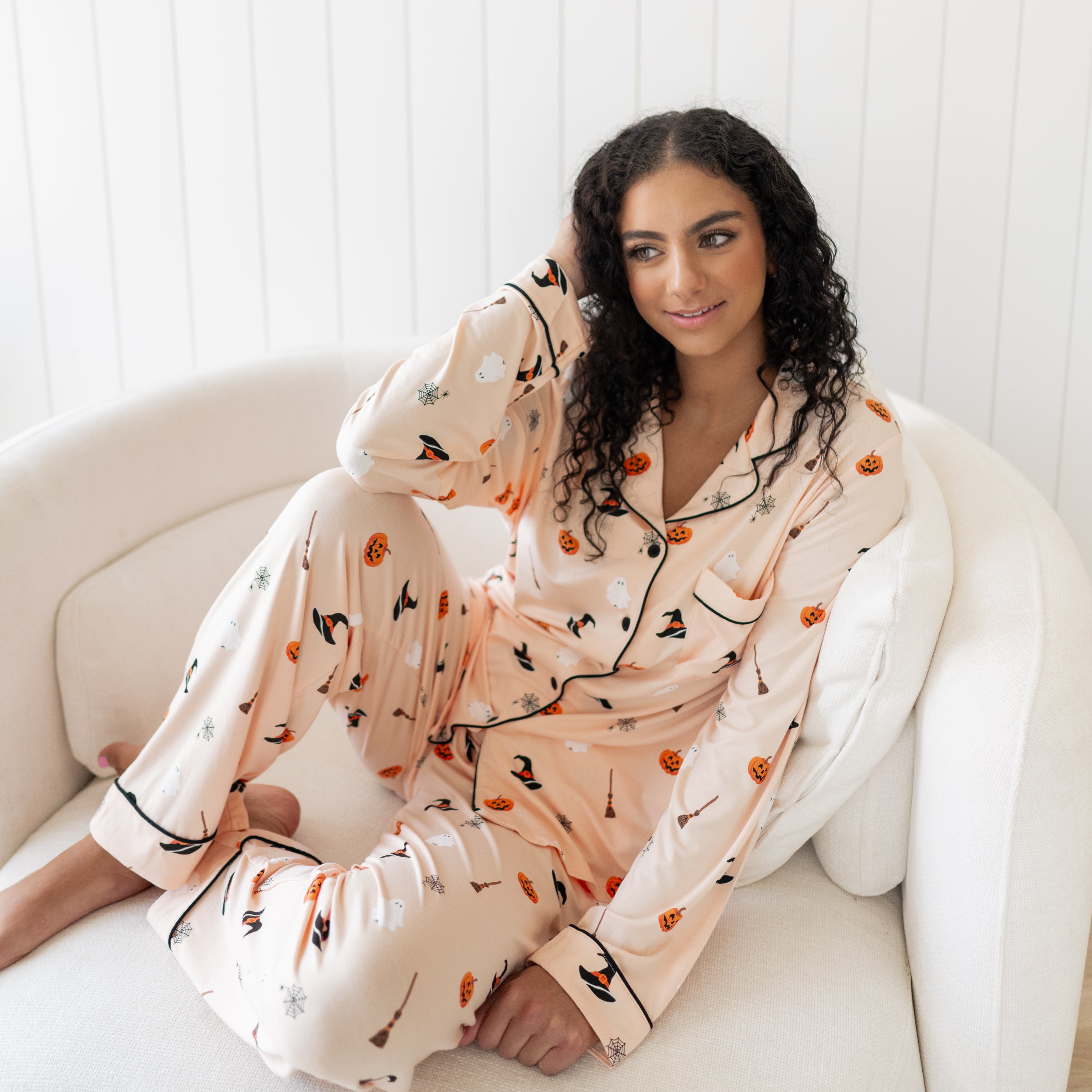 Woman wearing a Halloween-themed pajama set sitting on a white couch.
