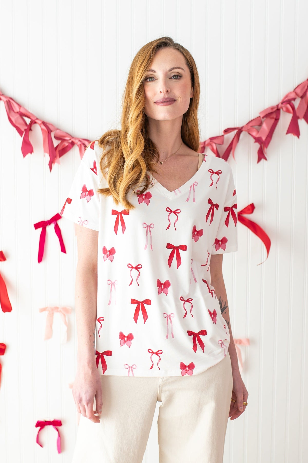 Woman standing in front of a streamer of bows while modeling the Bamboo Women's Relaxed Fit V-Neck in Big Love Bow